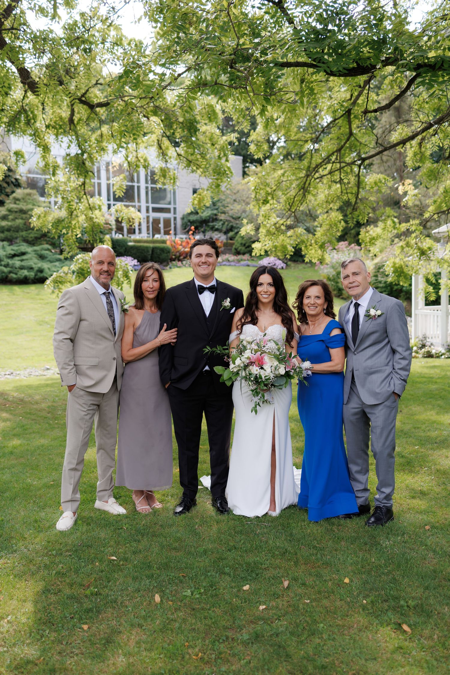 Wedding party members in coordinated formal attire pose for photos in a garden setting.