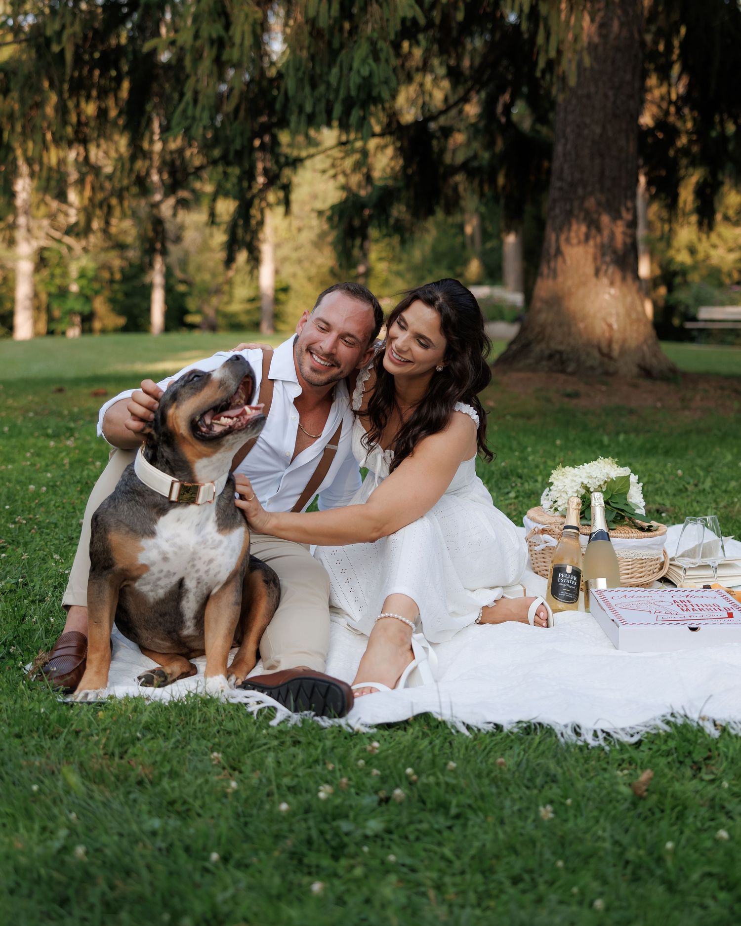 Couple in white clothing having a romantic picnic on grass with their dog.