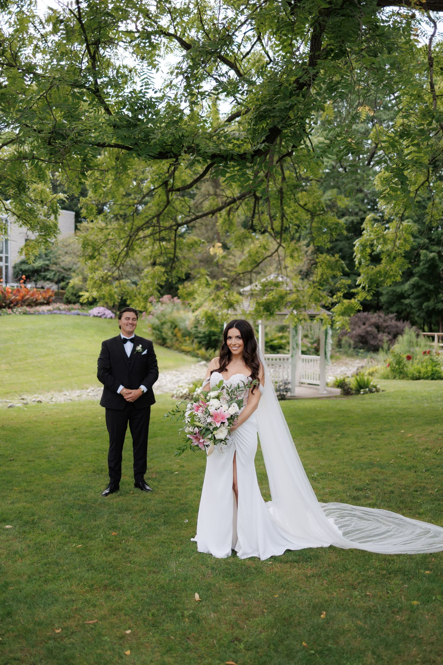 Wedding portraits in a scenic garden with a dramatic long veil trailing behind the couple.