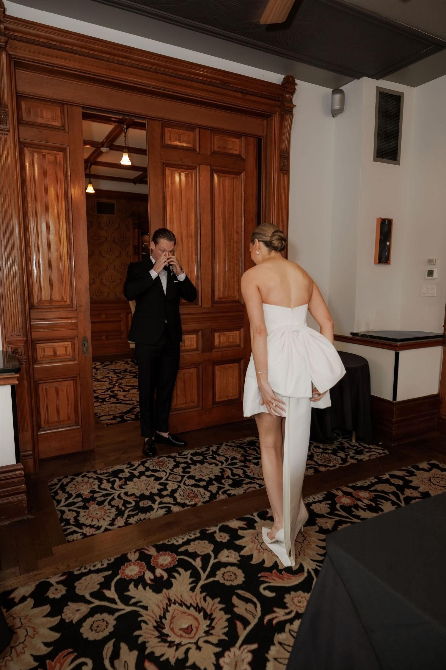 Emotional groom reacts seeing bride in strapless white mini dress during wedding first look reveal.