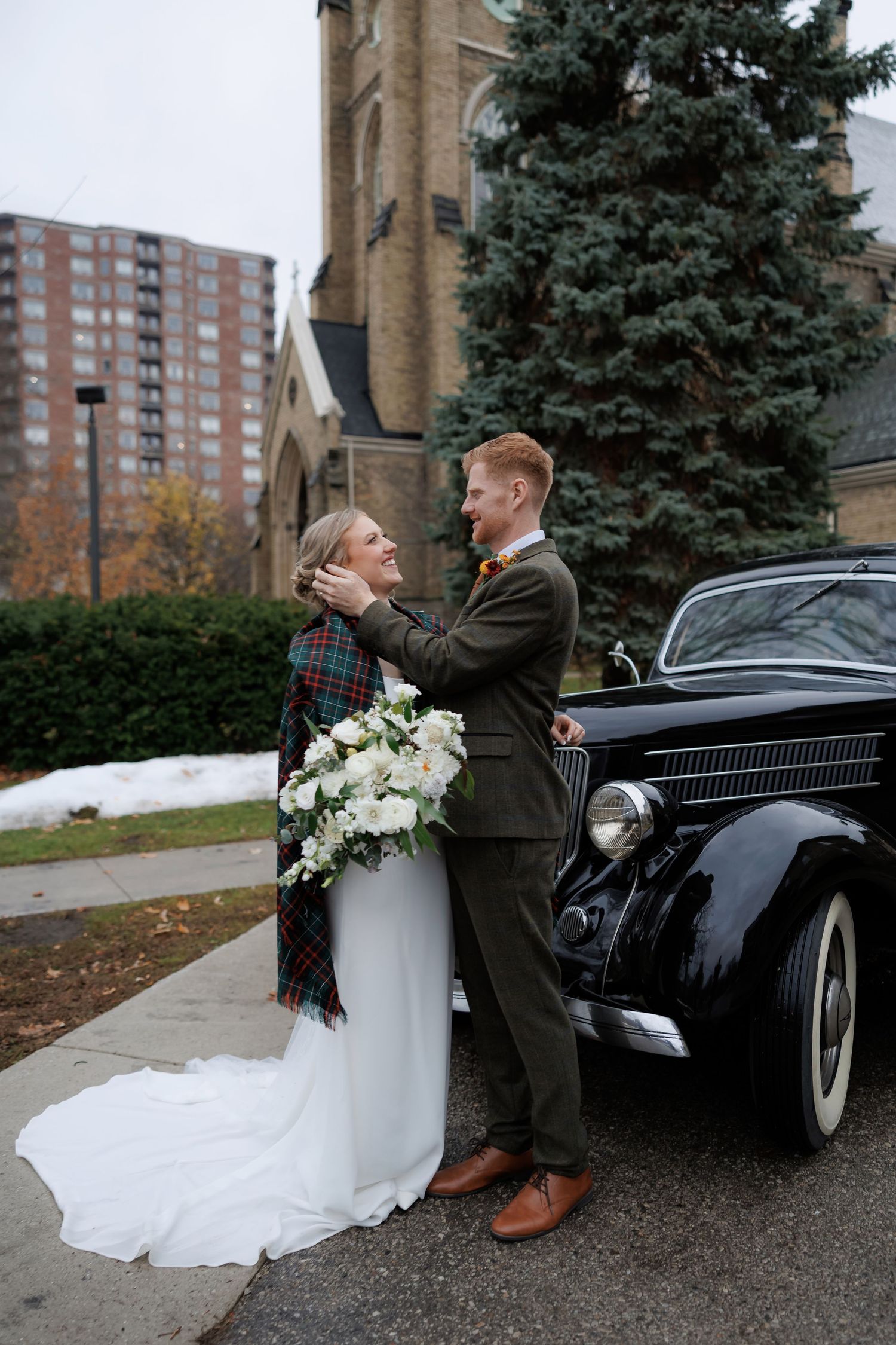 Romantic wedding portraits with vintage car outside church on winter day.