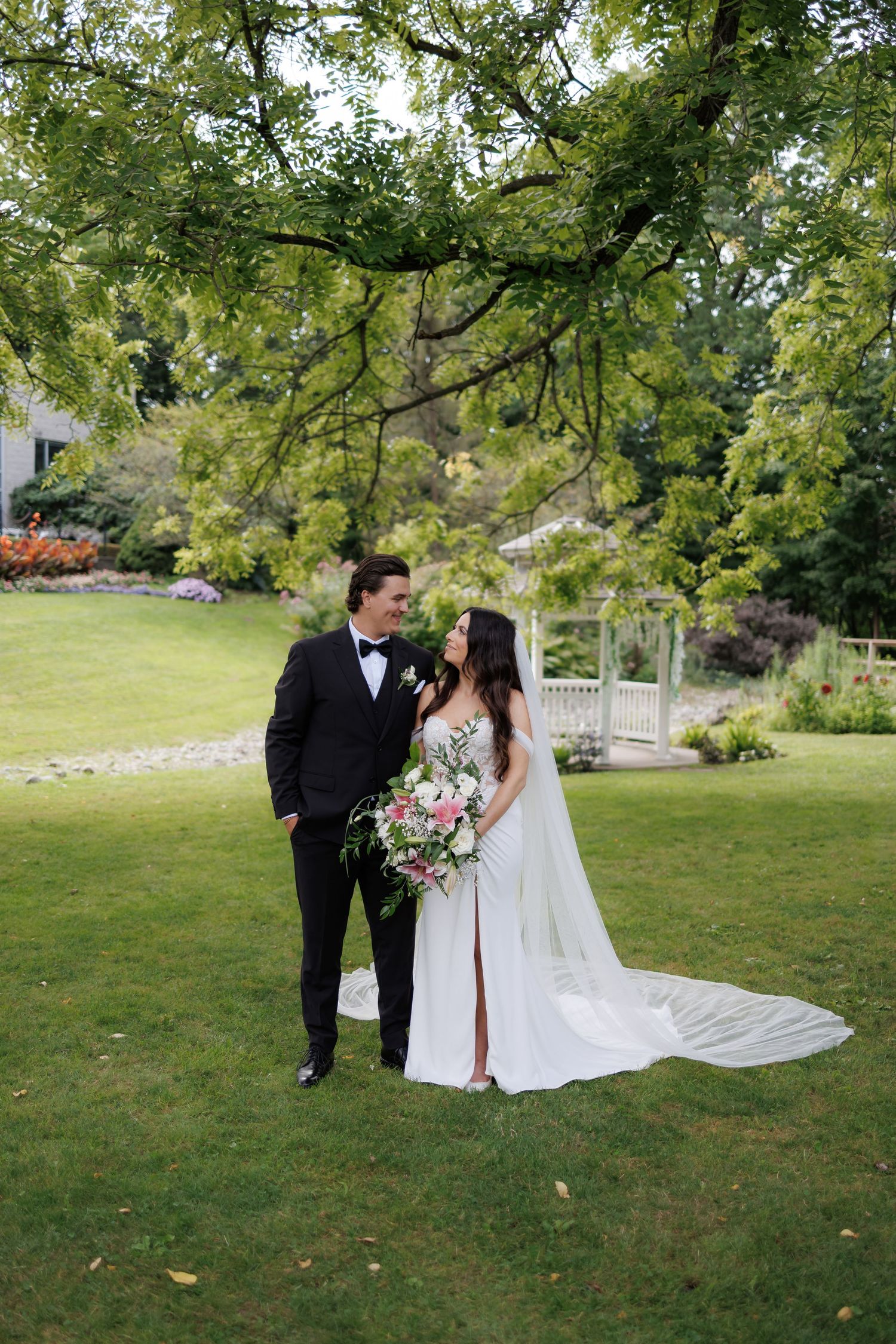 Wedding couple posing in lush garden setting with flowing white dress and bouquet.