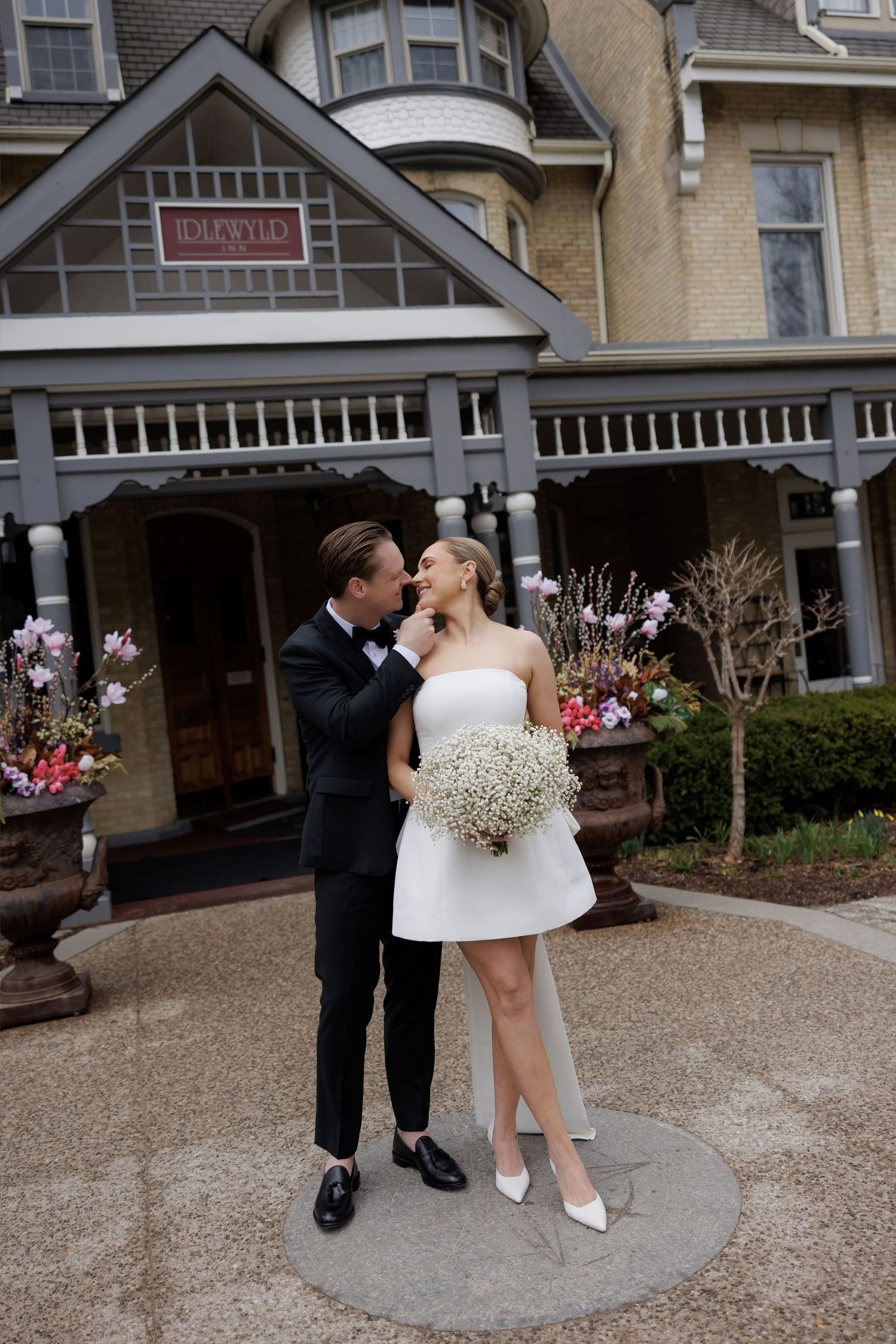 Bride and groom share romantic moment outside Idlewyld venue, bride holding white baby's breath bouquet.