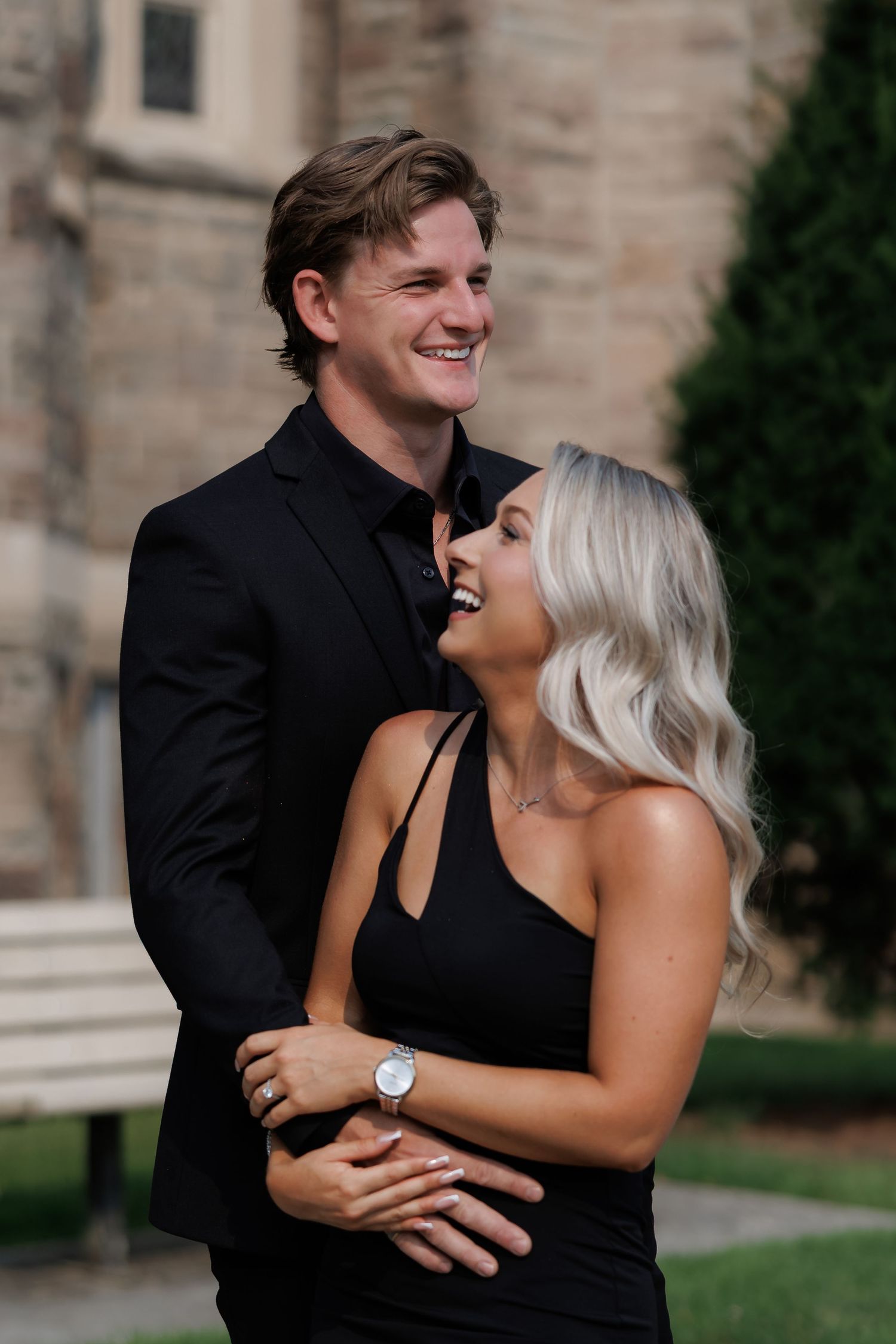 Couple sharing laughter and embracing in front of stone architecture.