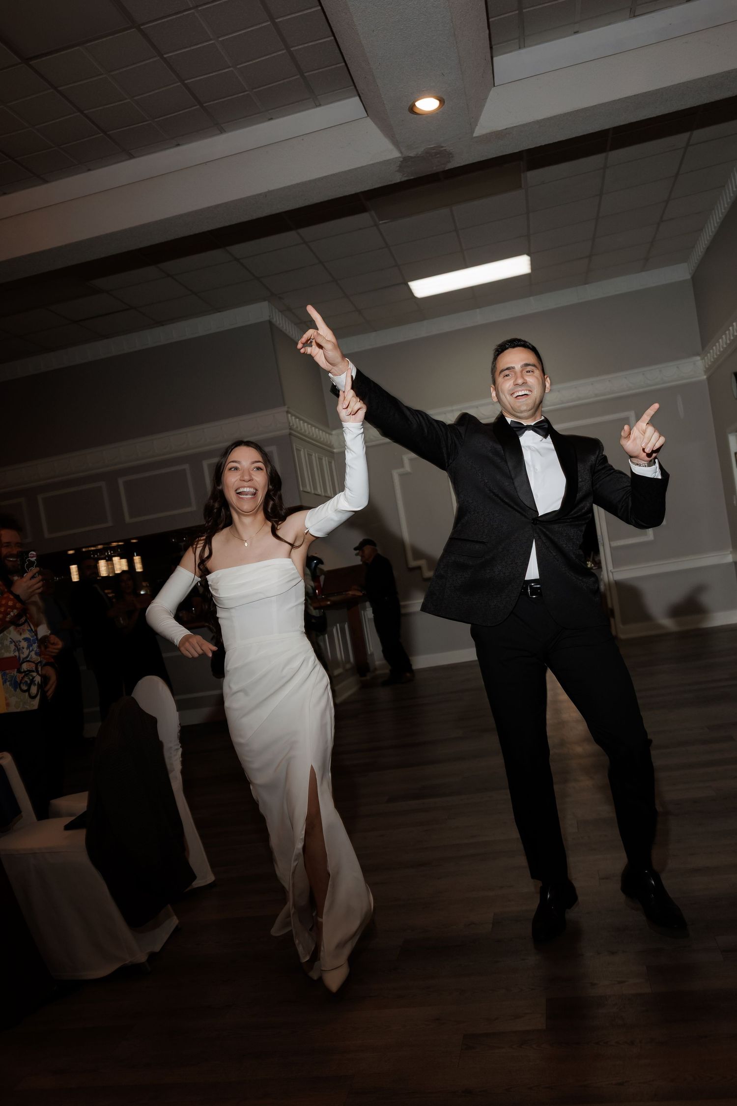 Wedding party members dancing and jumping on wooden dance floor at reception.