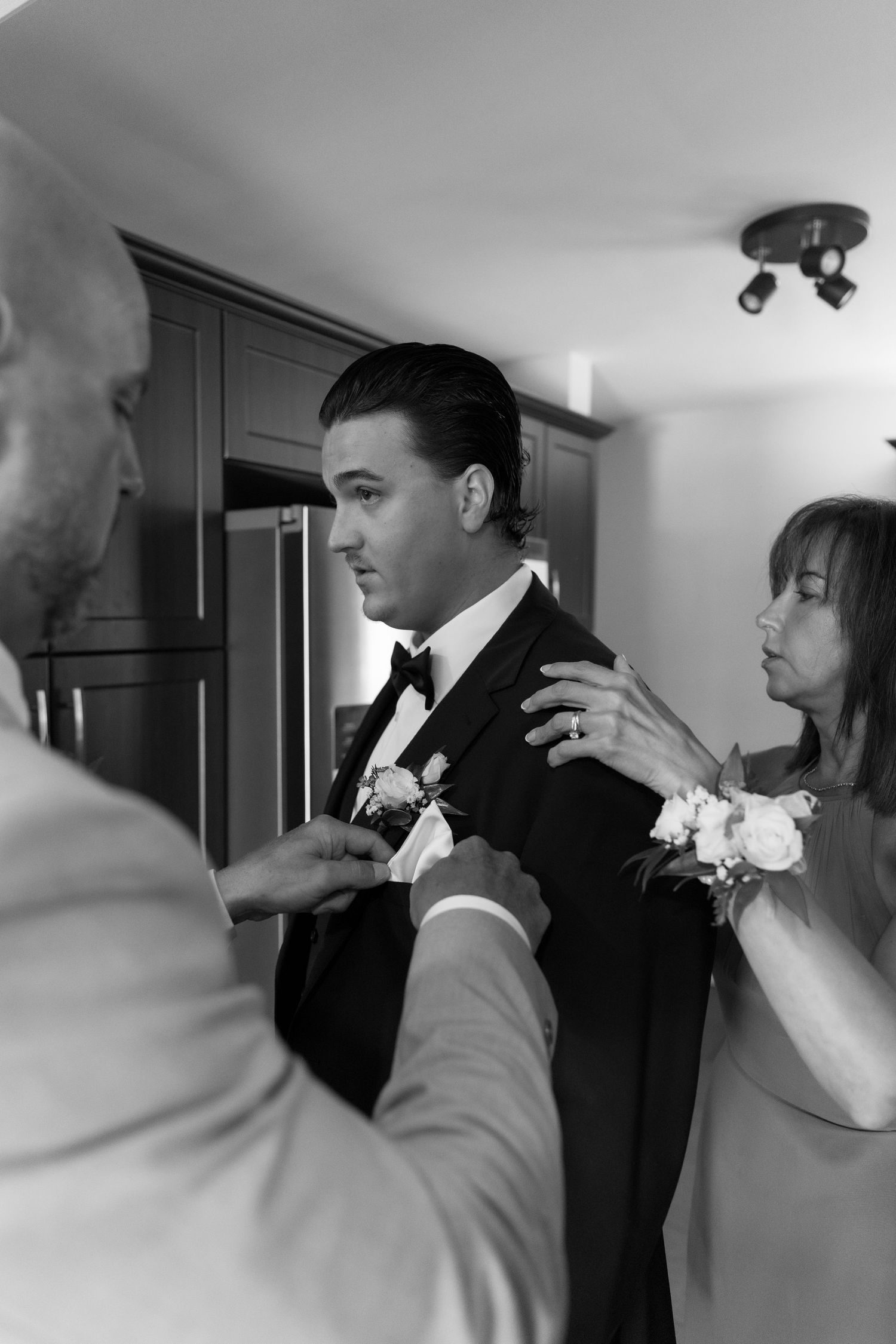 Black and white photo of wedding preparations with boutonniere being pinned.