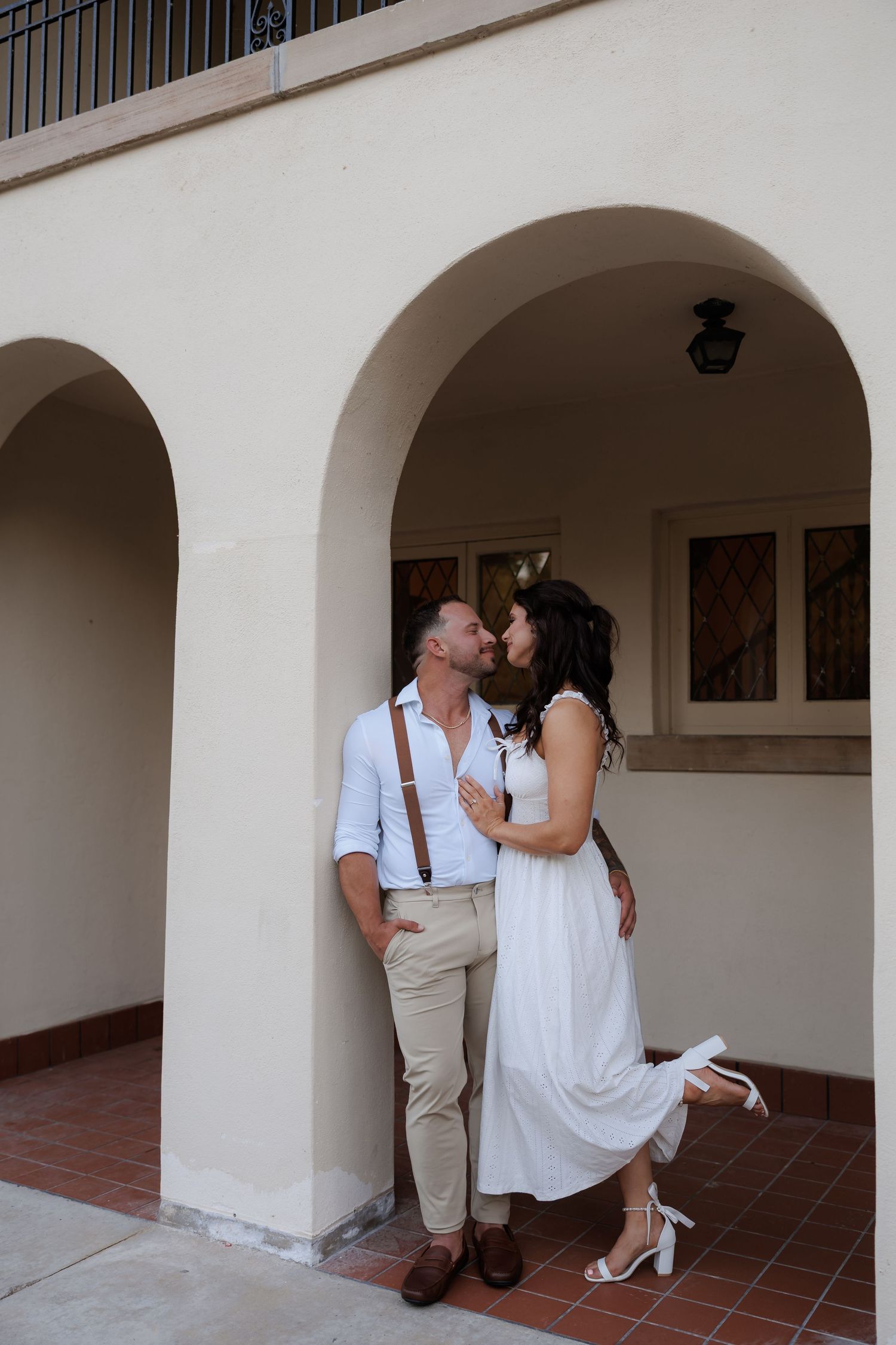 Romantic couple posing under white archways of Mediterranean style building.