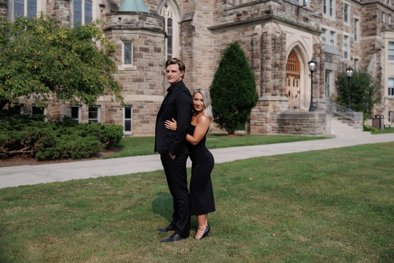 Couple in formal wear photographed from distance near historic stone building.