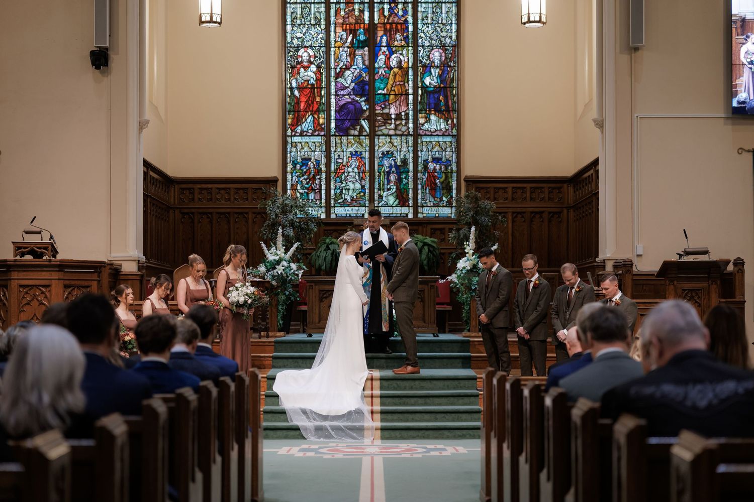 Wedding ceremony in progress inside historic church with wooden pews and stained glass windows.