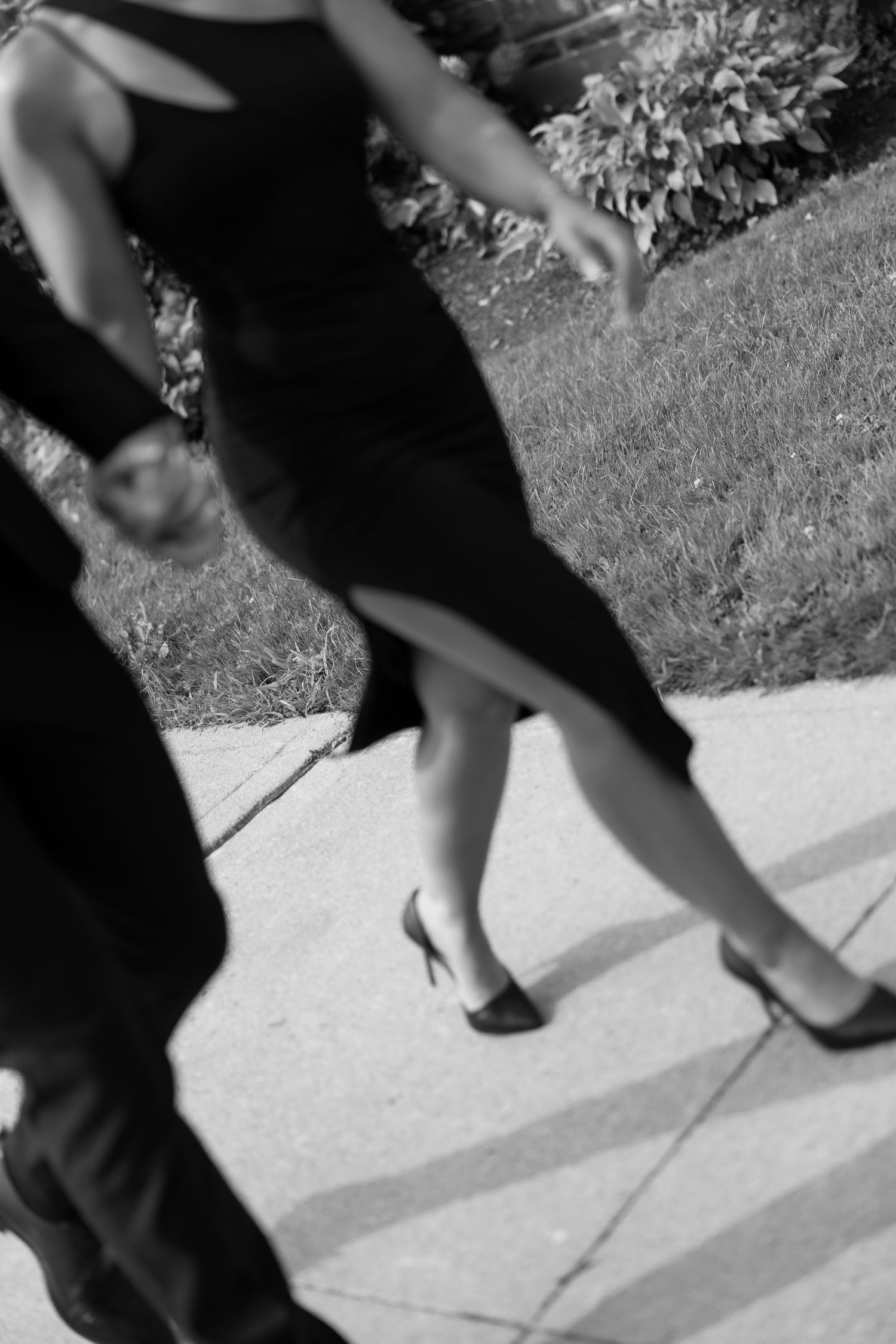 Black and white photo showing feet and legs walking on a sidewalk.