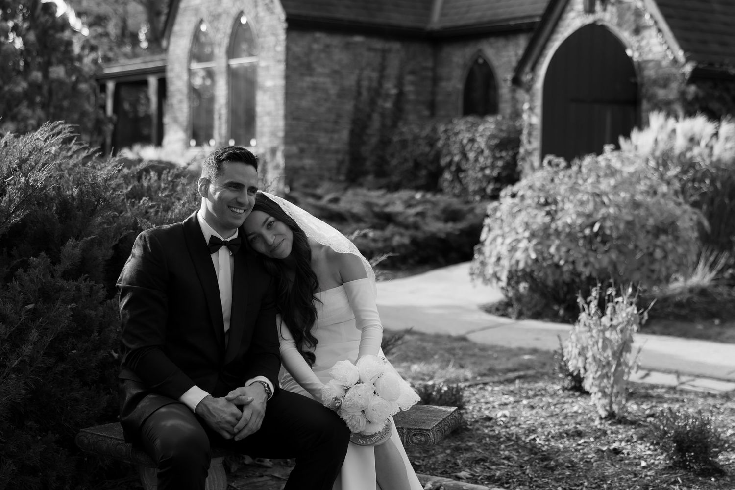 Black and white wedding portraits captured in a garden setting with stone church architecture.