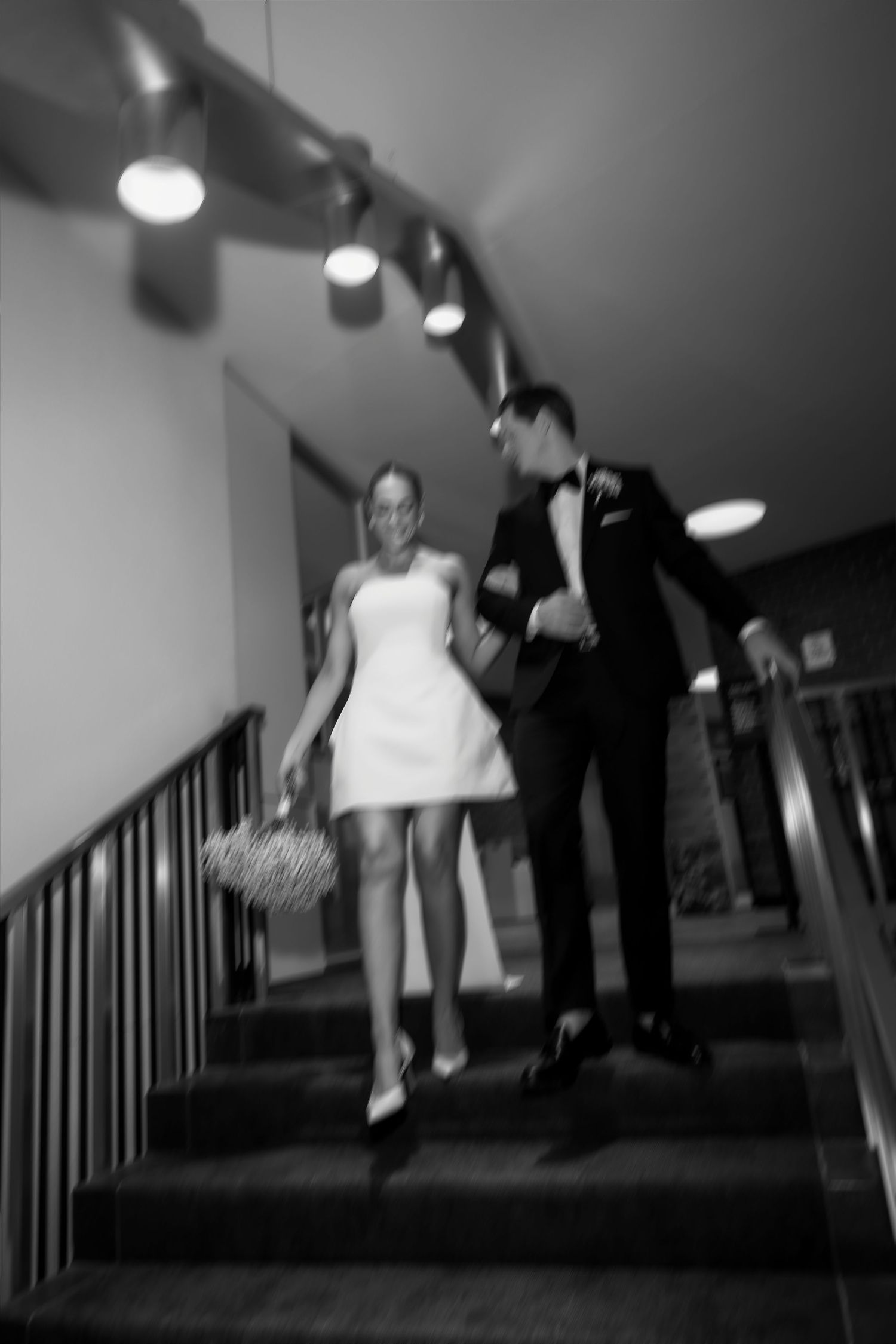 Bride and groom descend staircase hand in hand in a dreamy motion-blur black and white wedding photo.