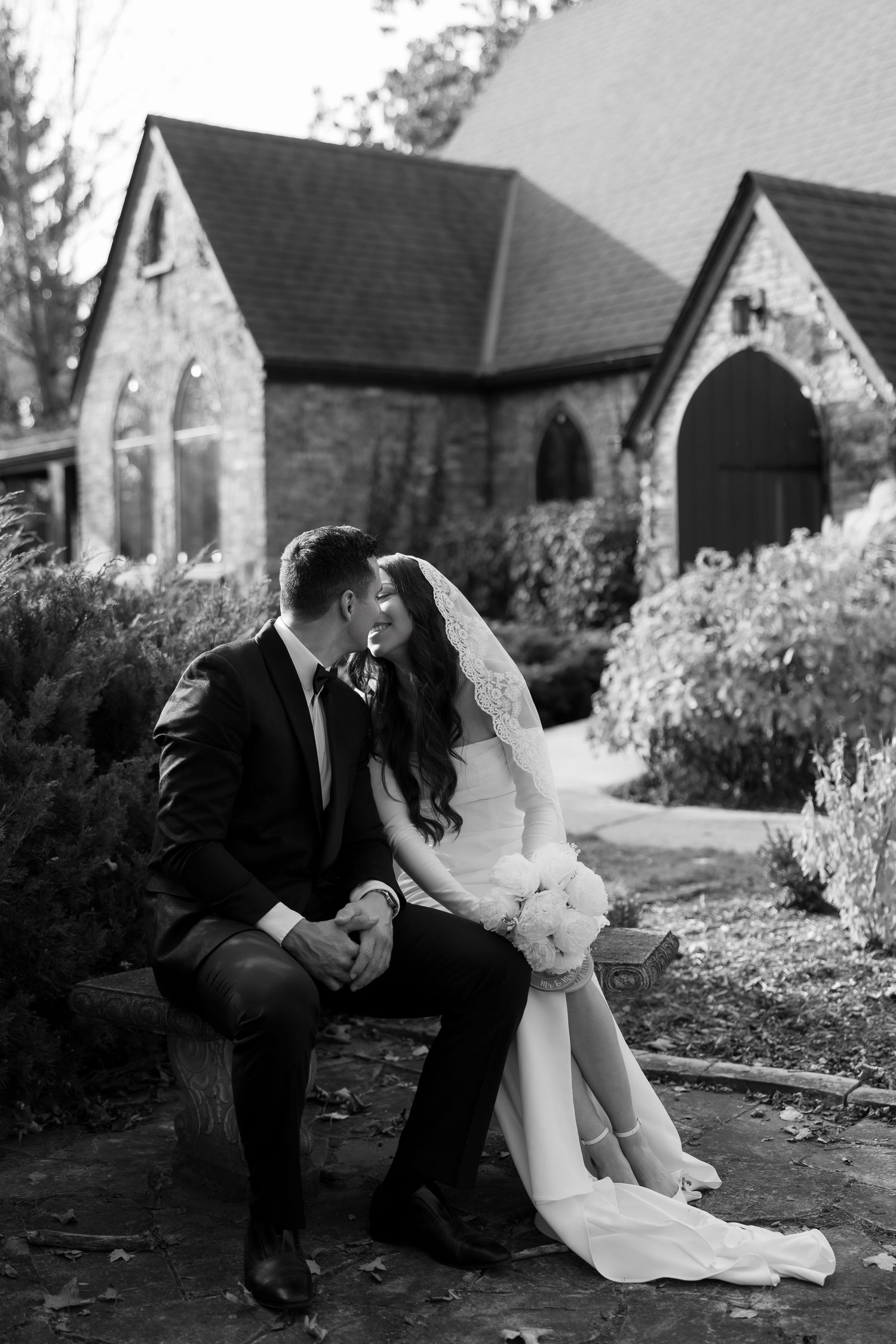 Intimate black and white wedding portraits taken on church grounds with romantic poses.