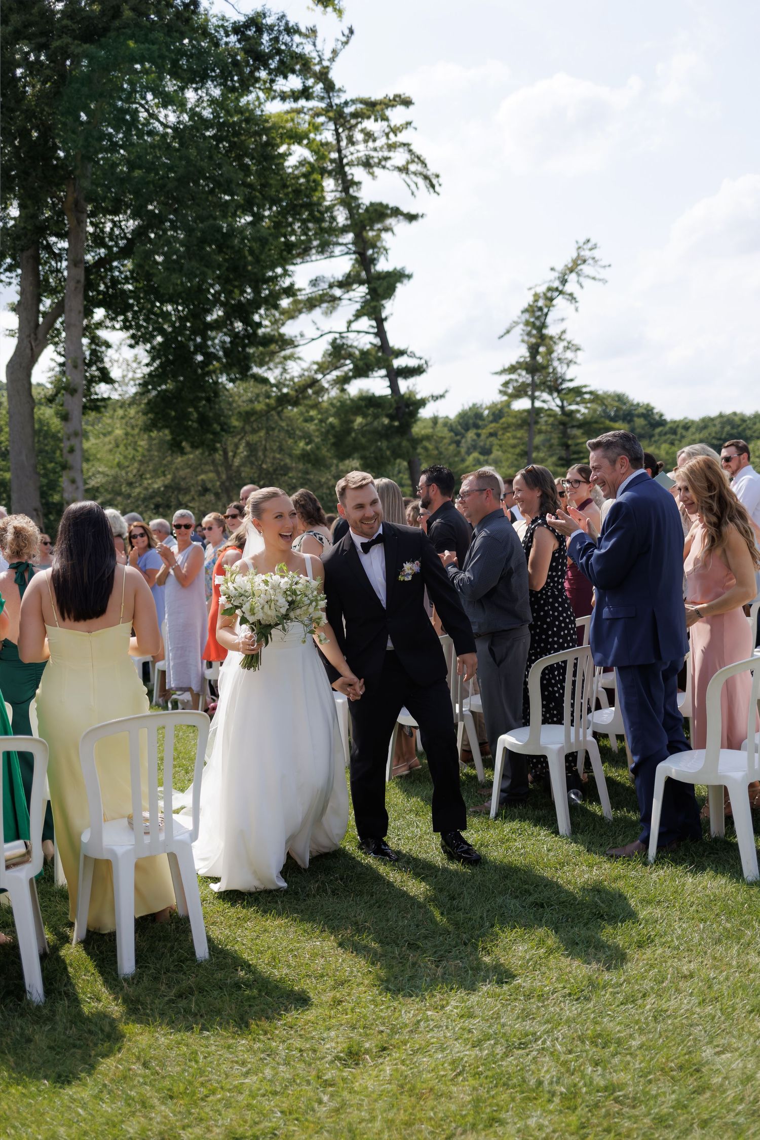 Bride and groom walking back down the aisle after outdoor wedding ceremony among cheering guests.