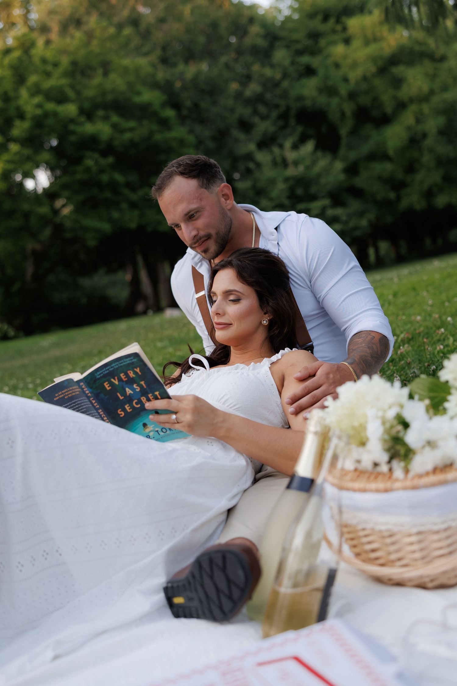 Couple relaxing on blanket with picnic basket and drinks in outdoor garden.