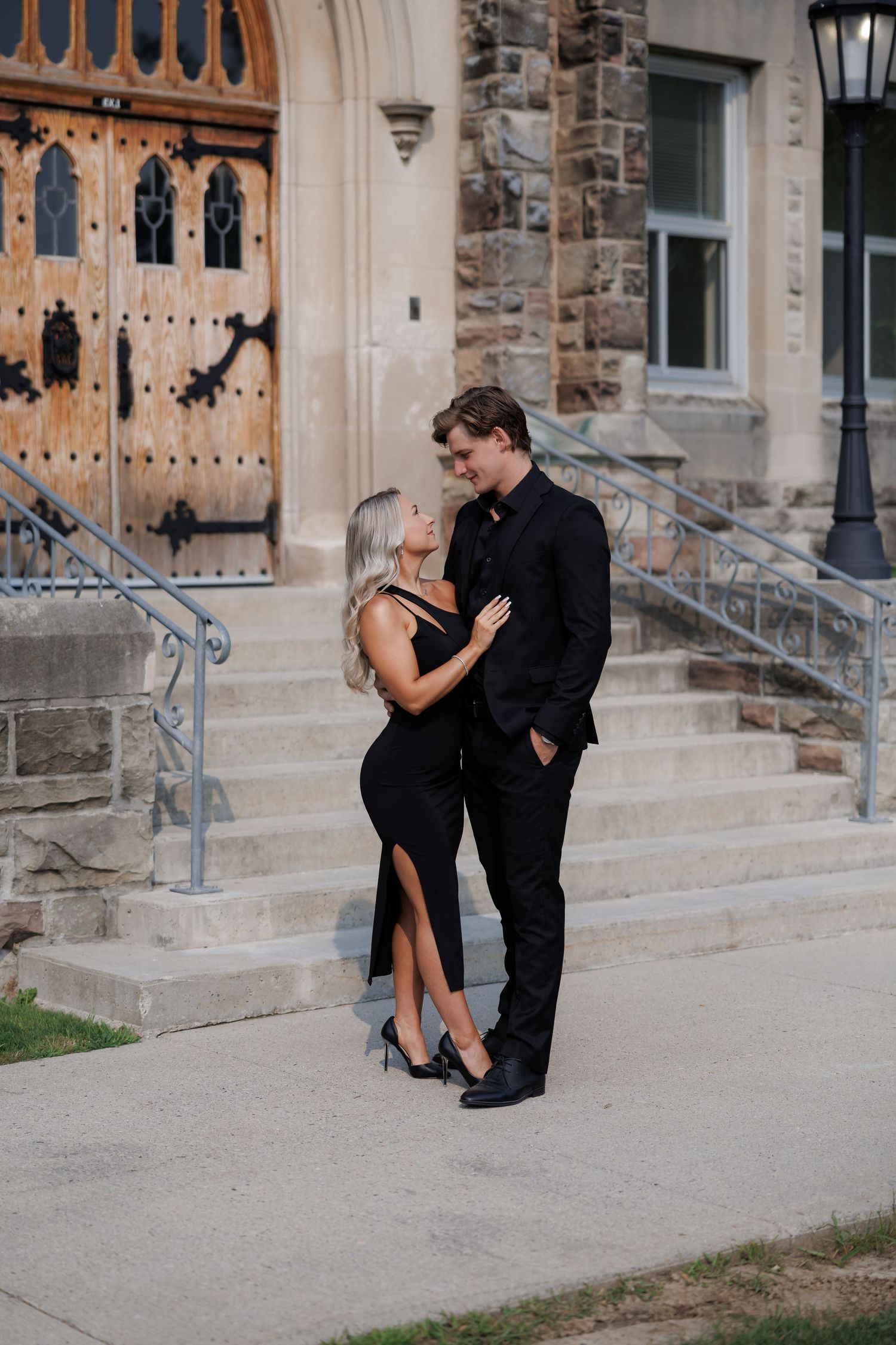 Couple in formal wear posing together on stone steps of historic building.