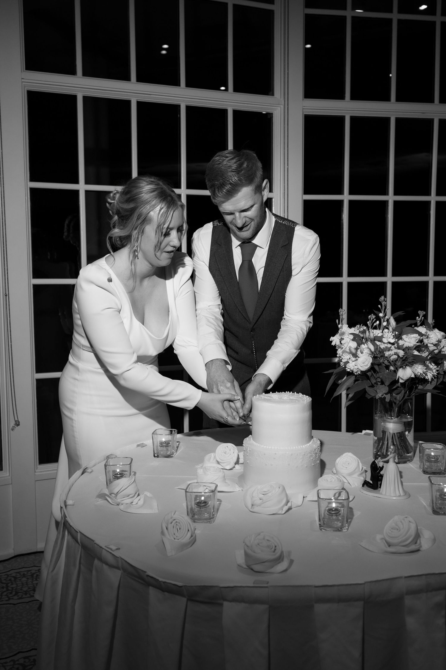 Wedding couple cutting their traditional white tiered cake together.
