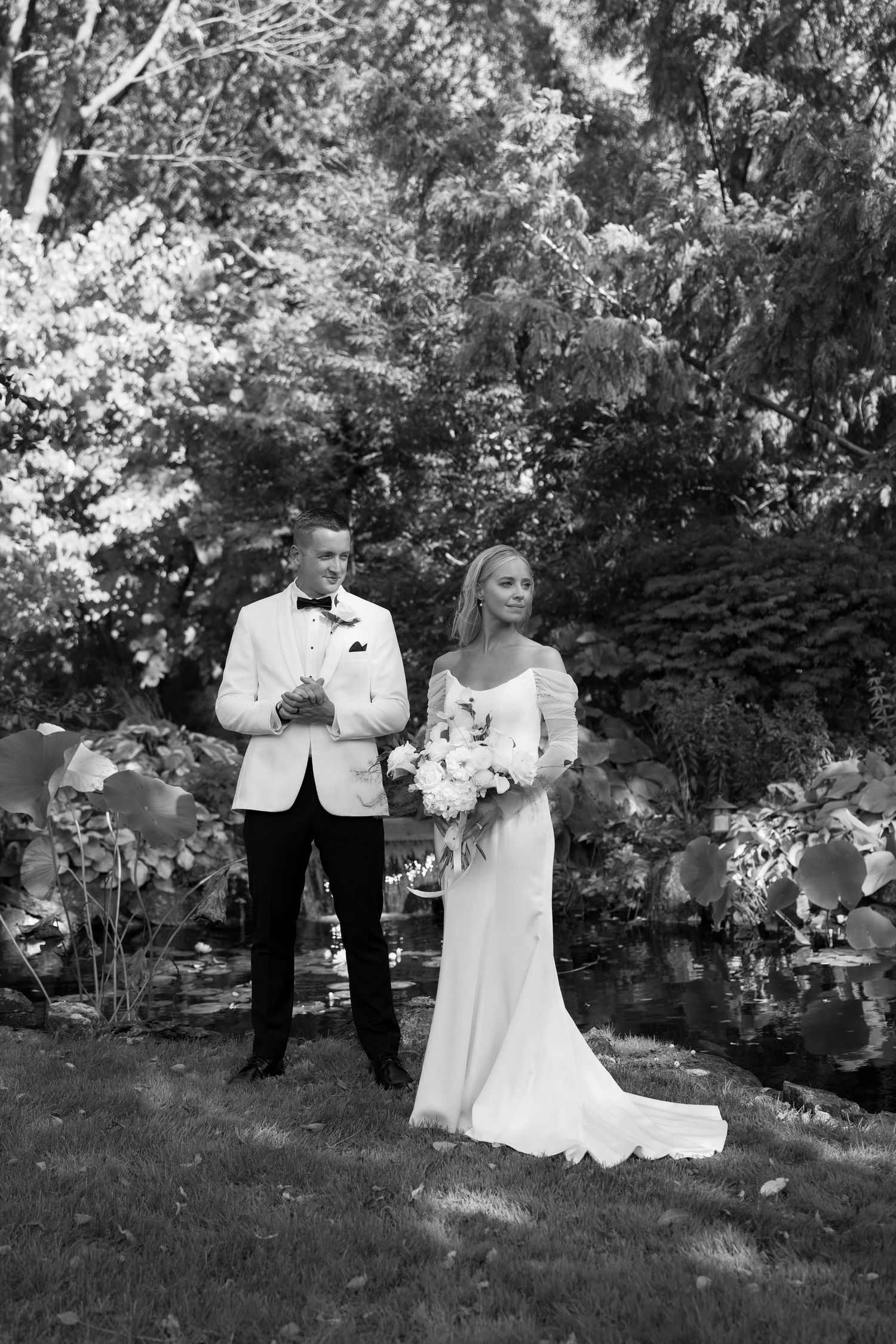 Elegant wedding couple poses in a lush garden setting with natural greenery and trees.