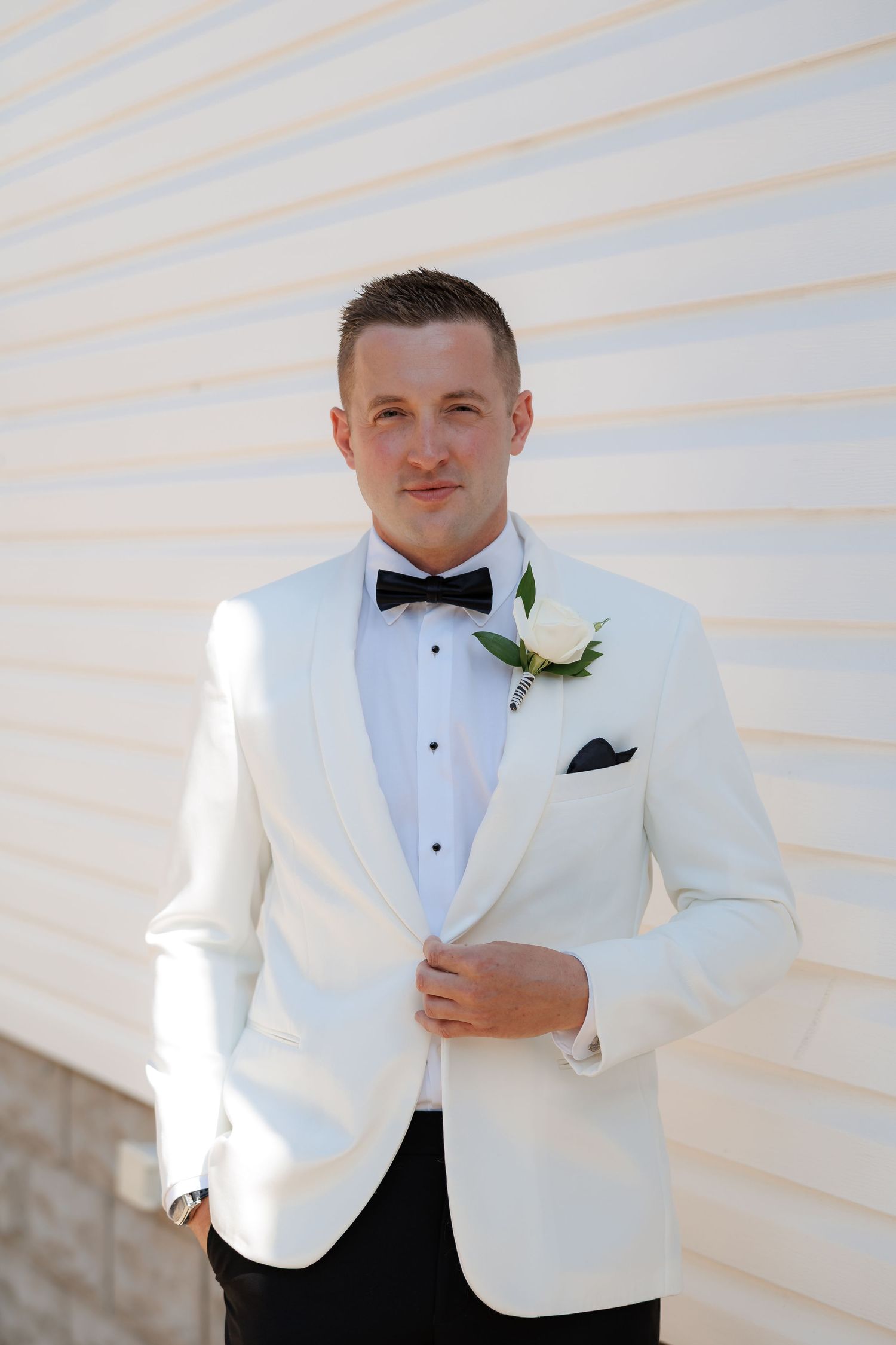 White tuxedo jacket with black bow tie detail shown in formal wedding attire.