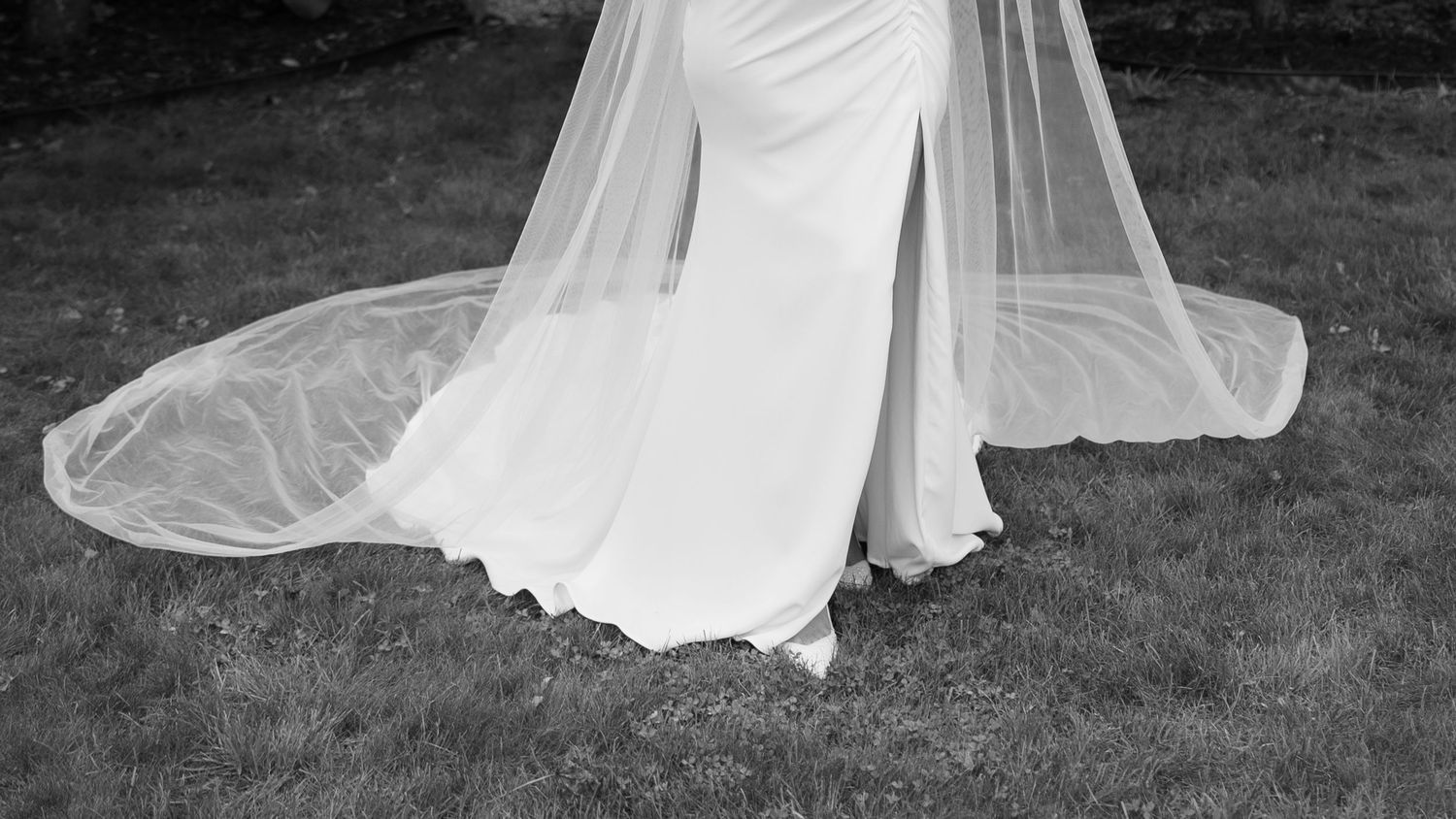 Flowing white wedding dress train spread across grass in an artistic composition.
