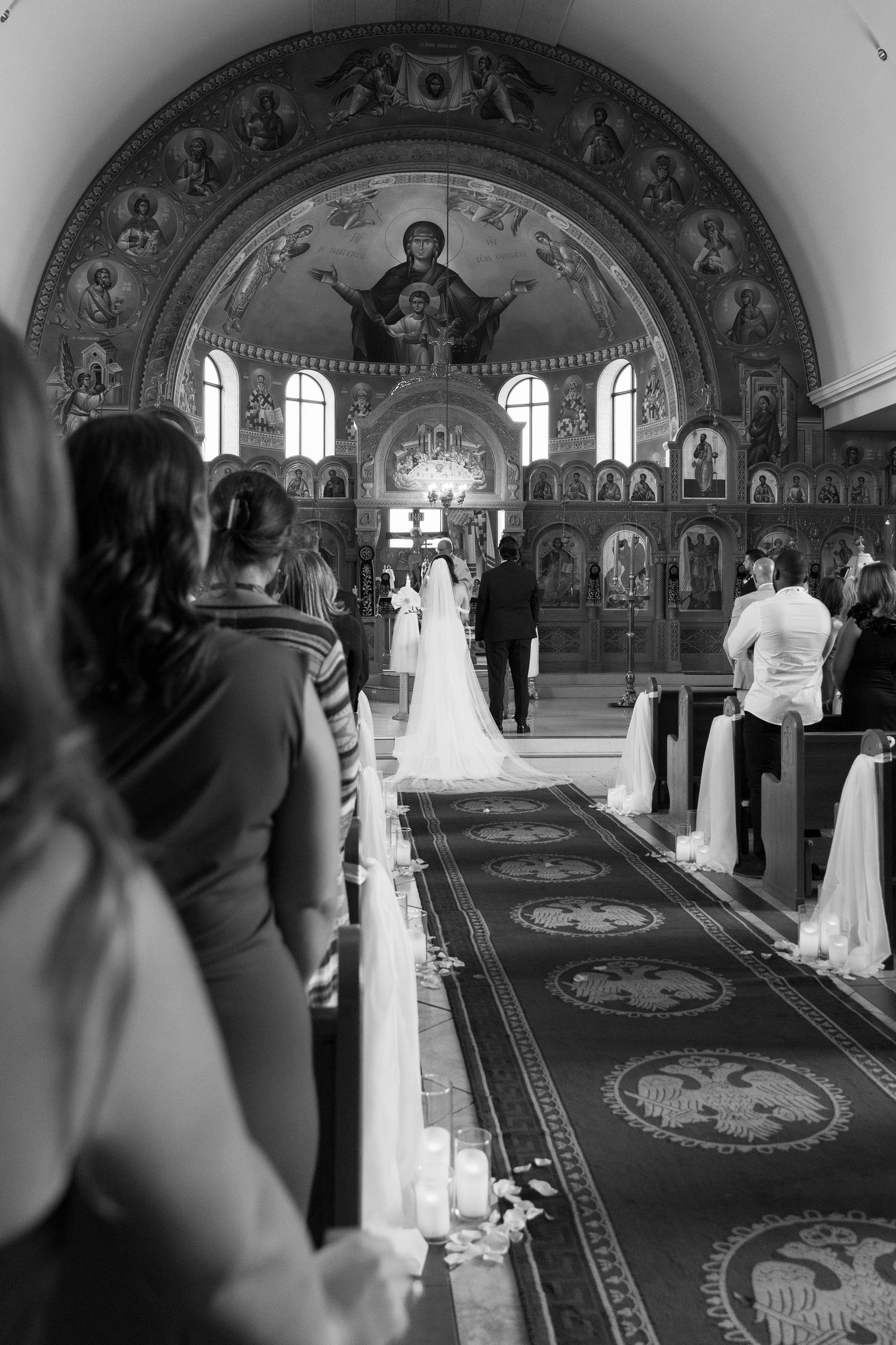 Black and white wedding ceremony in Orthodox church with dramatic lighting and religious iconography.