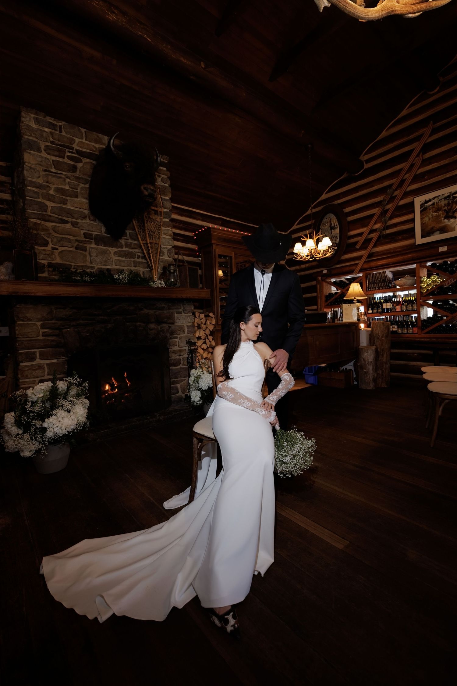 Bride and groom share romantic moment in rustic log cabin venue with stone fireplace during wedding reception.