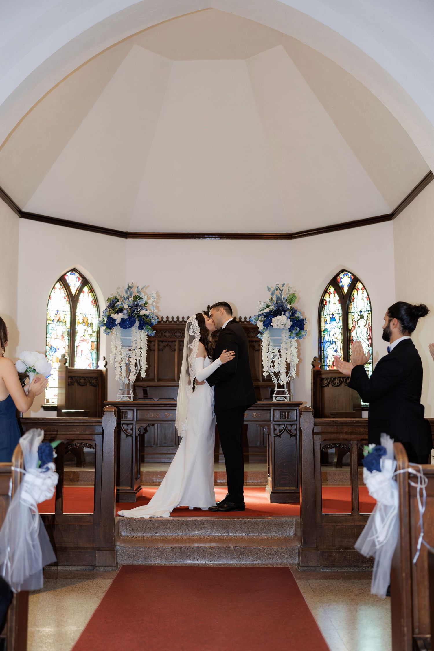 Wedding ceremony in progress inside church sanctuary with arched ceiling and stained glass.
