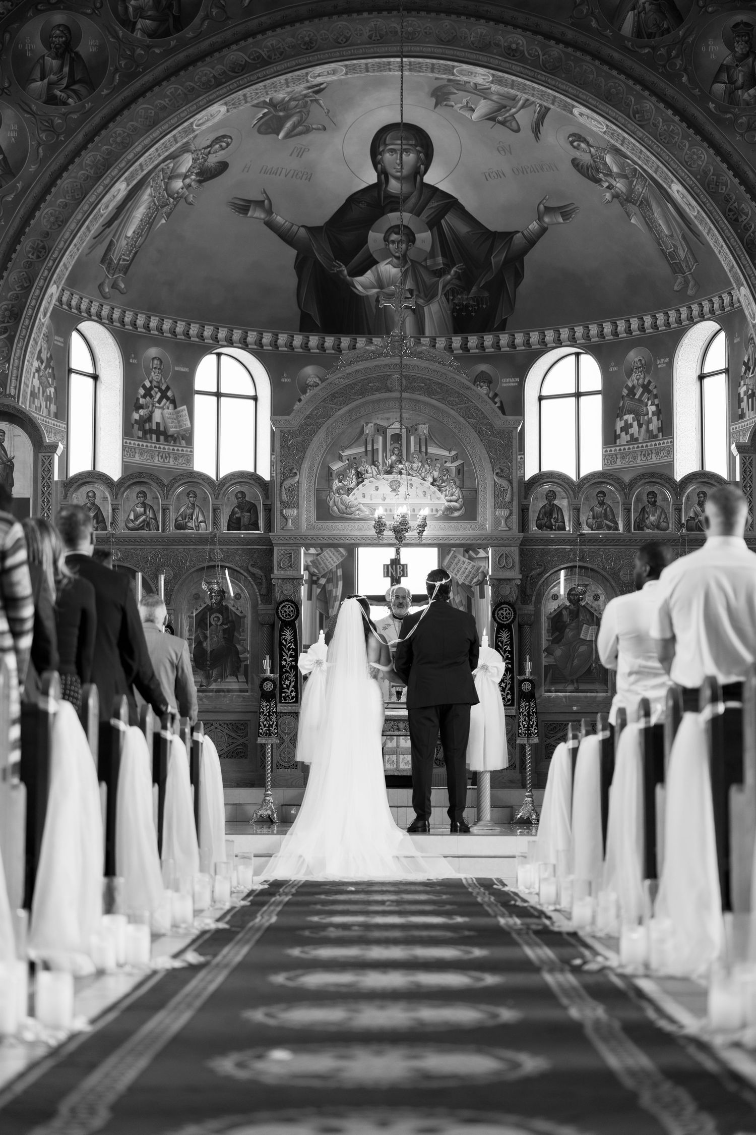 Orthodox church wedding ceremony in ornate sanctuary with decorated pews and arched ceiling.
