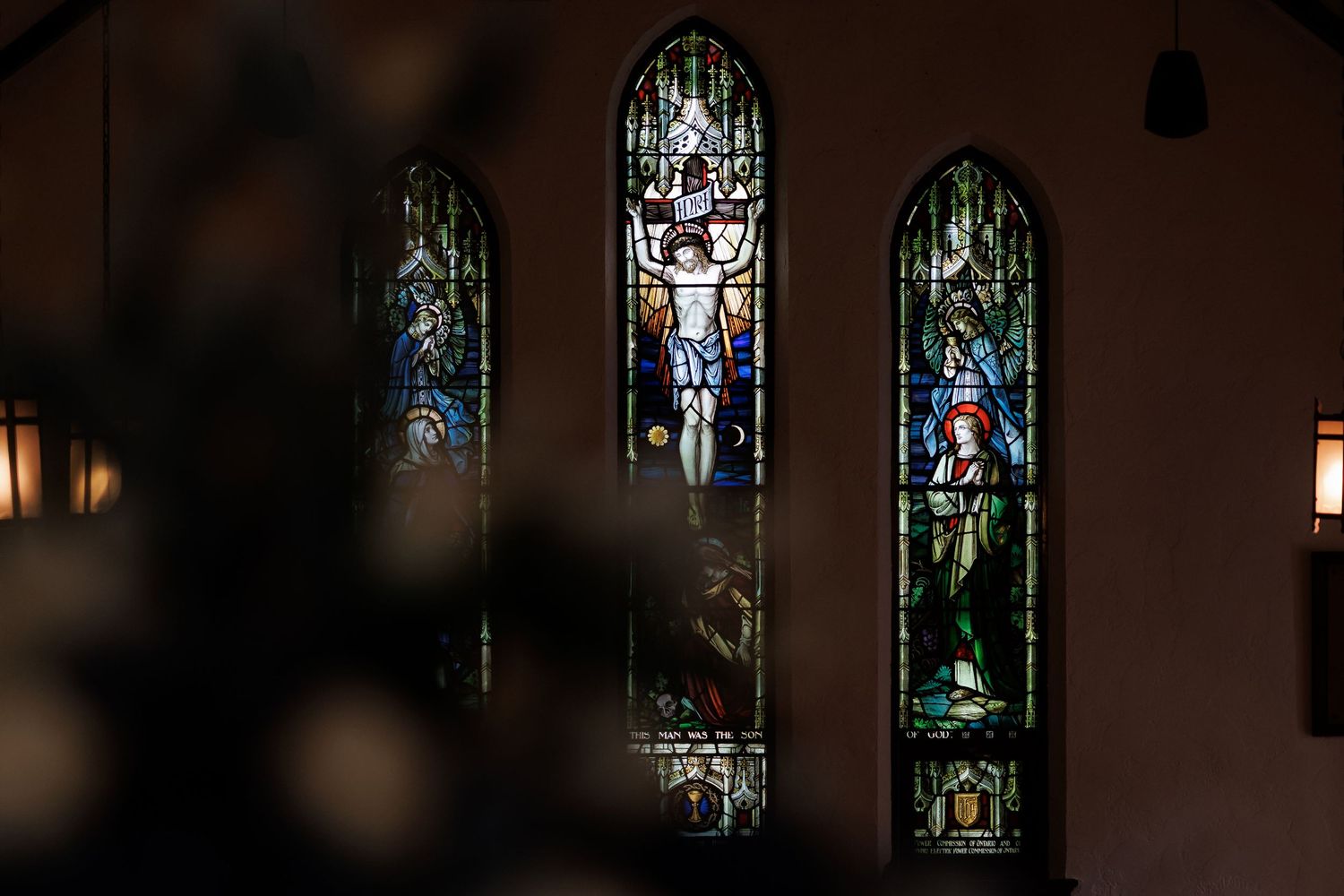 Row of stained glass windows in dark church interior creates dramatic lighting.