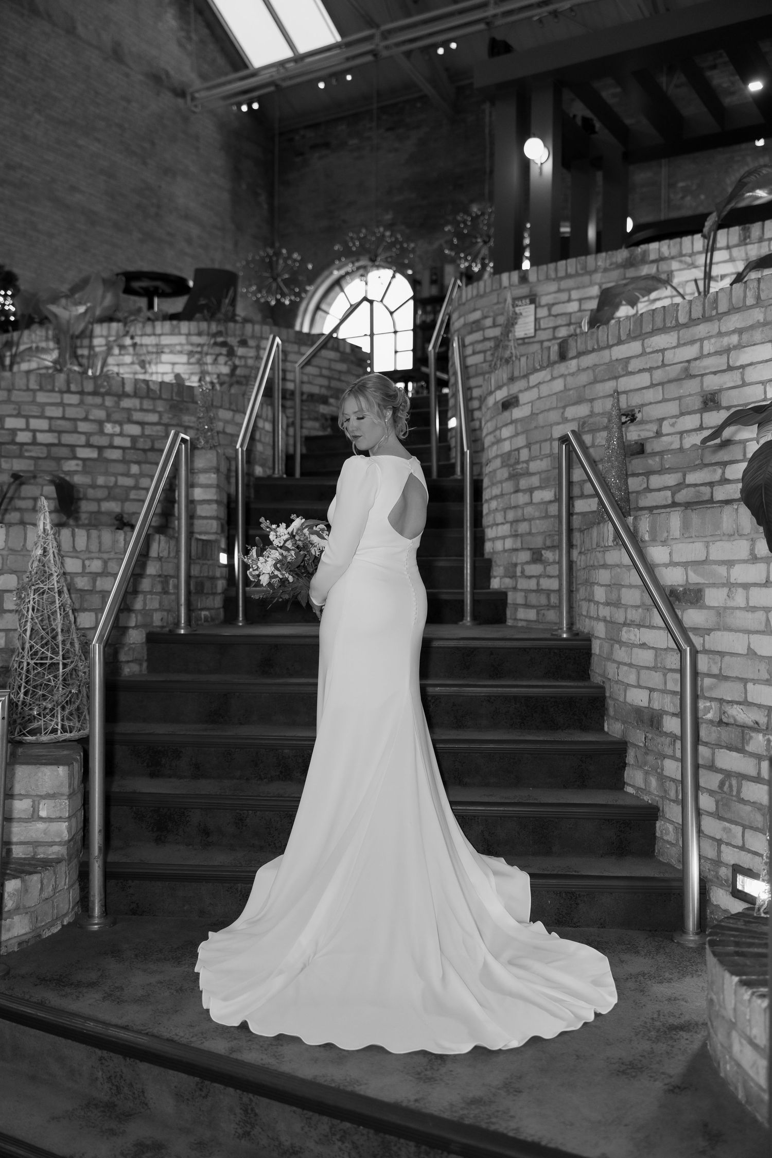 Wedding dress displayed against brick wall backdrop with elegant train flowing.