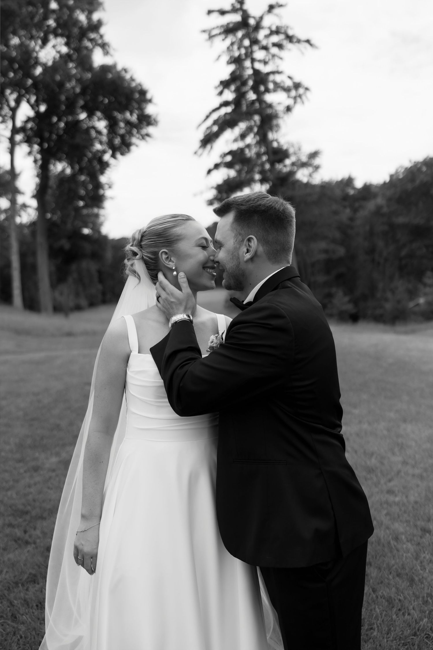 Black and white photo of groom tenderly holding brides face as they share a kiss outdoors.
