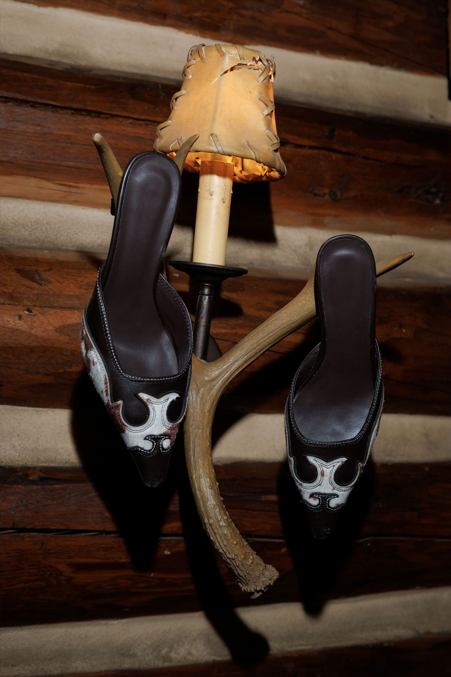 Western cowboy mule heels displayed on antler wall sconce against rustic log cabin wall.