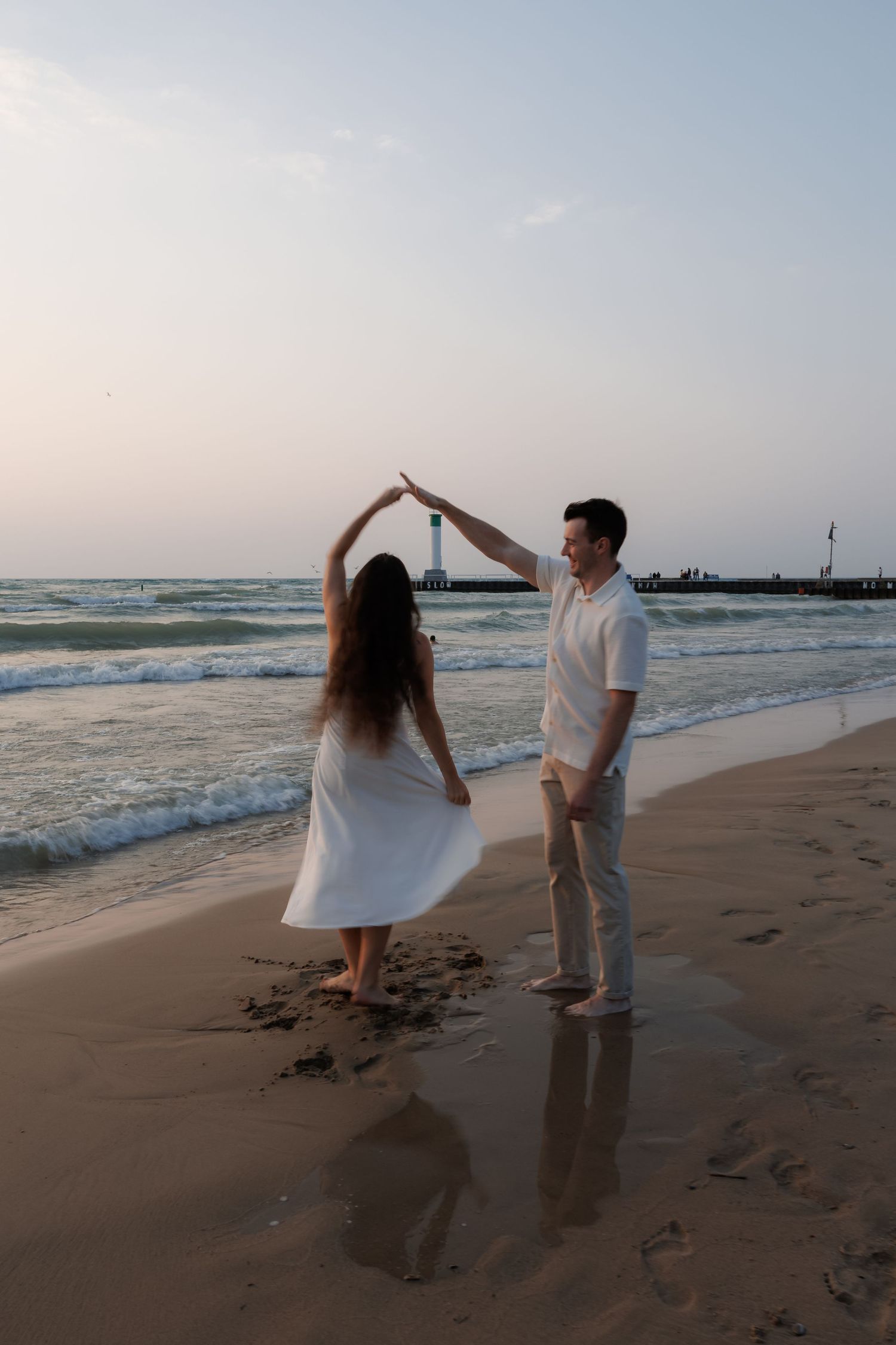 A couple dances together on a sandy beach at sunset with ocean waves in the background.