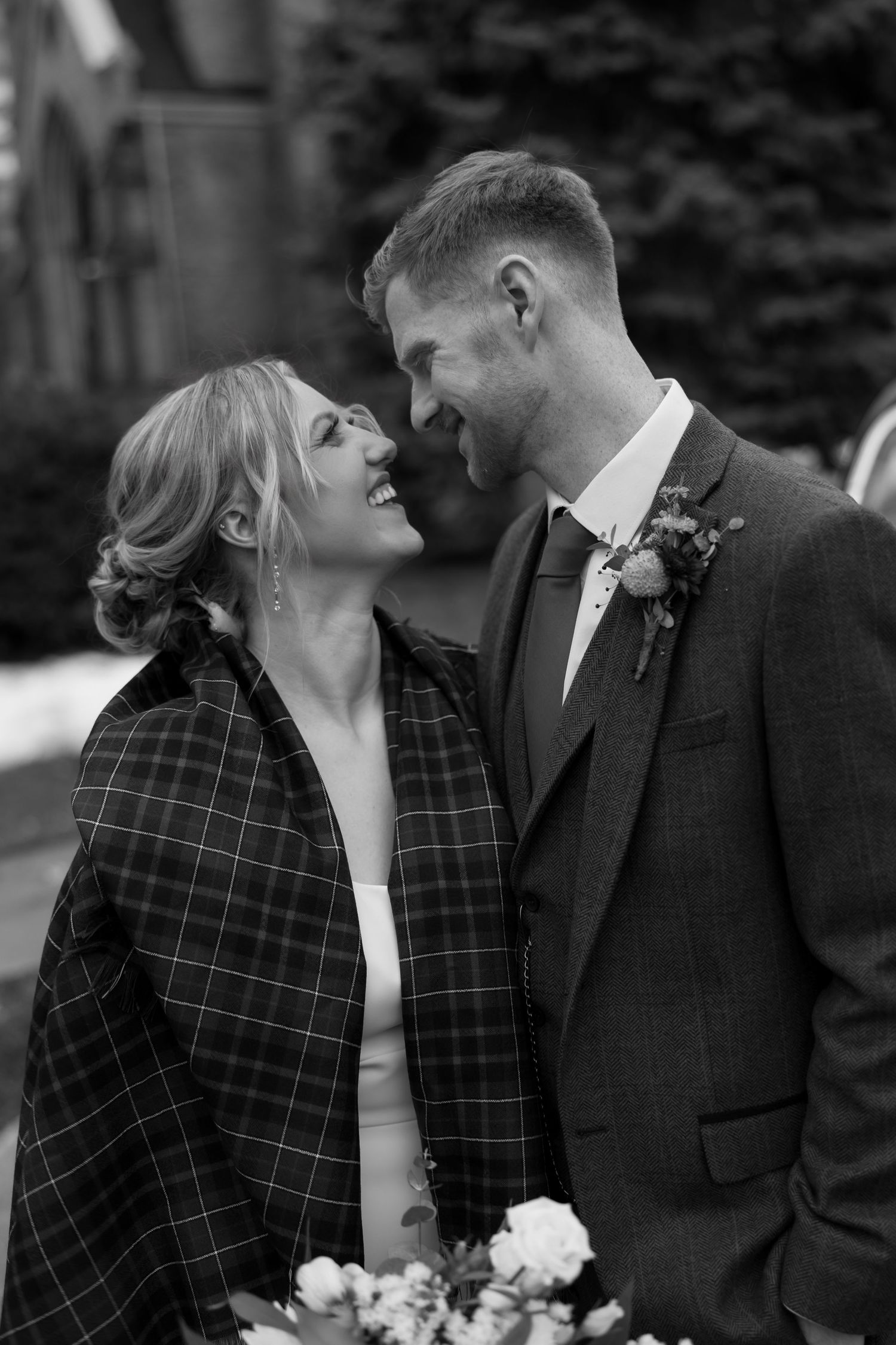 Intimate moment between couple in plaid and formal wear outside church.