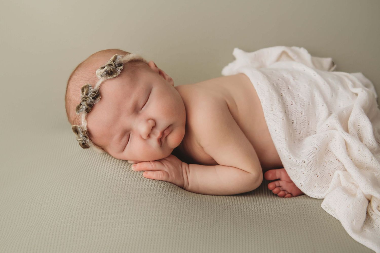 A sleeping newborn girl on a light green backdrop with a bow headband, taken by a Tri-Cities newborn photographer.