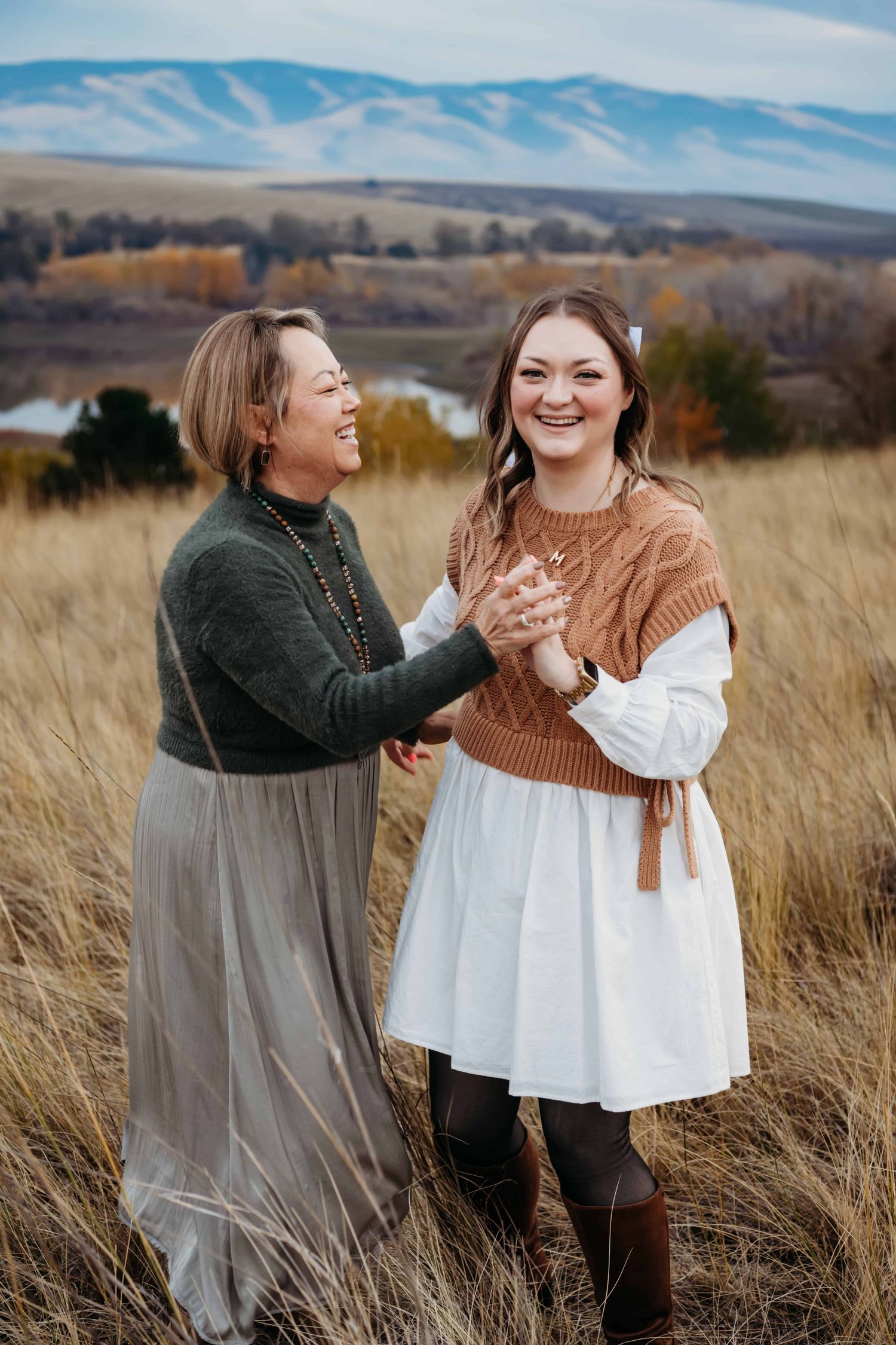 A mother and her daughter holding hands with a lake and mountains in the background.