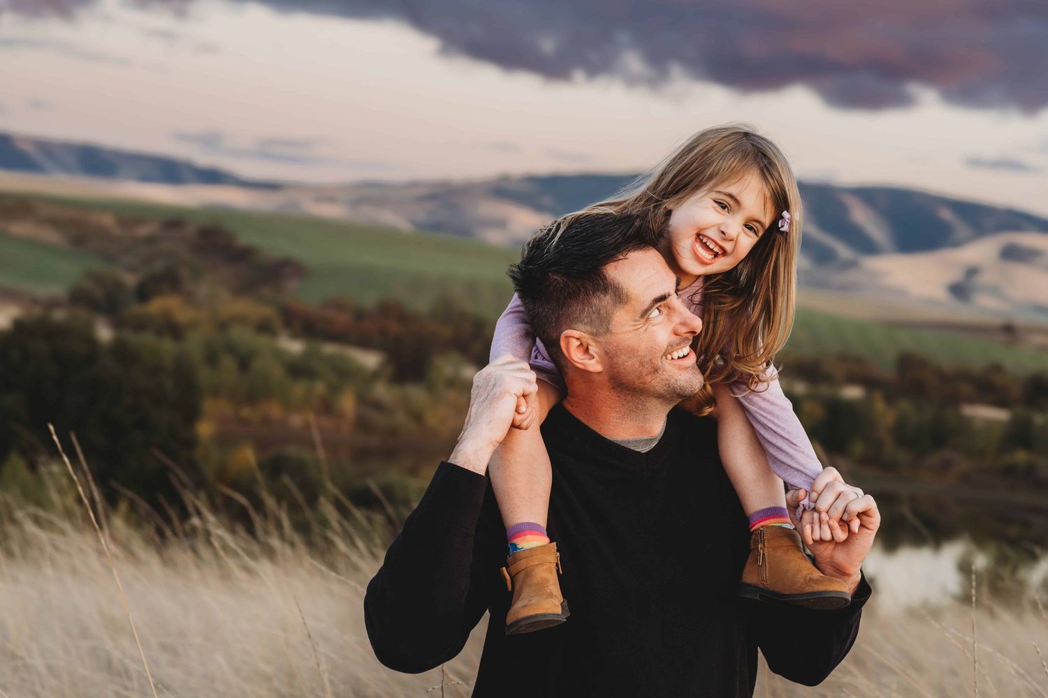 A girl sitting on her dad's shoulders and laughing as he looks at her, during sunset at Bennington Lake in Walla Walla.