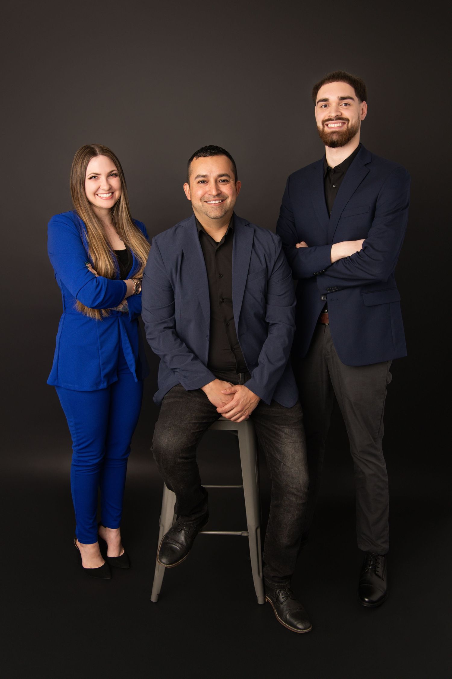 A group of three Walla Walla real estate agents standing for a professional headshot on a black backdrop.