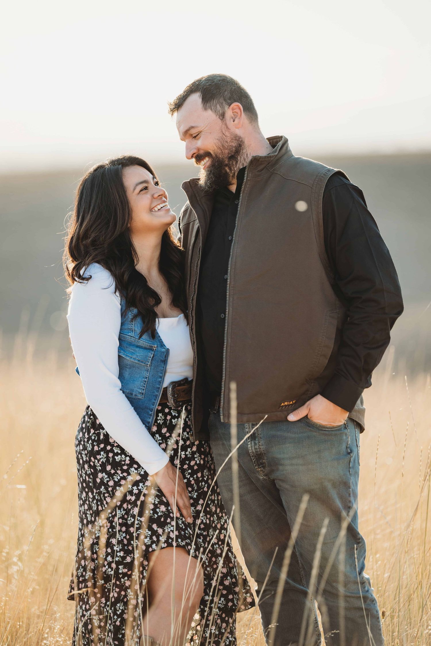 Walla Walla couples photographer capturing a couple smiling at each other in tall golden grass at sunset.
