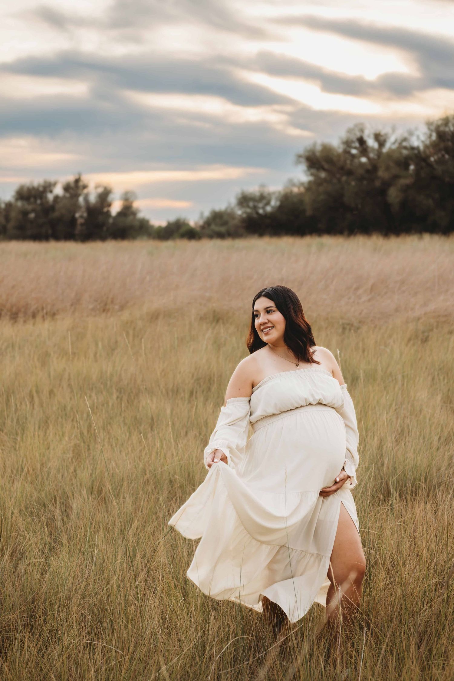 A pregnant woman standing in a field wearing a cream colored dress during a maternity photoshoot in Walla Walla.