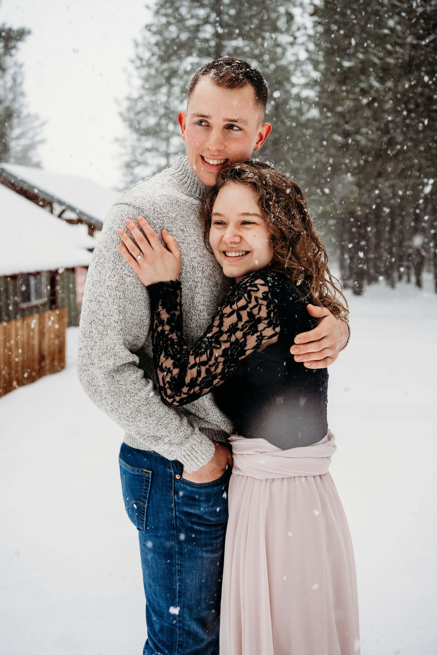 A couple hugging and looking away from the camera in the snow.