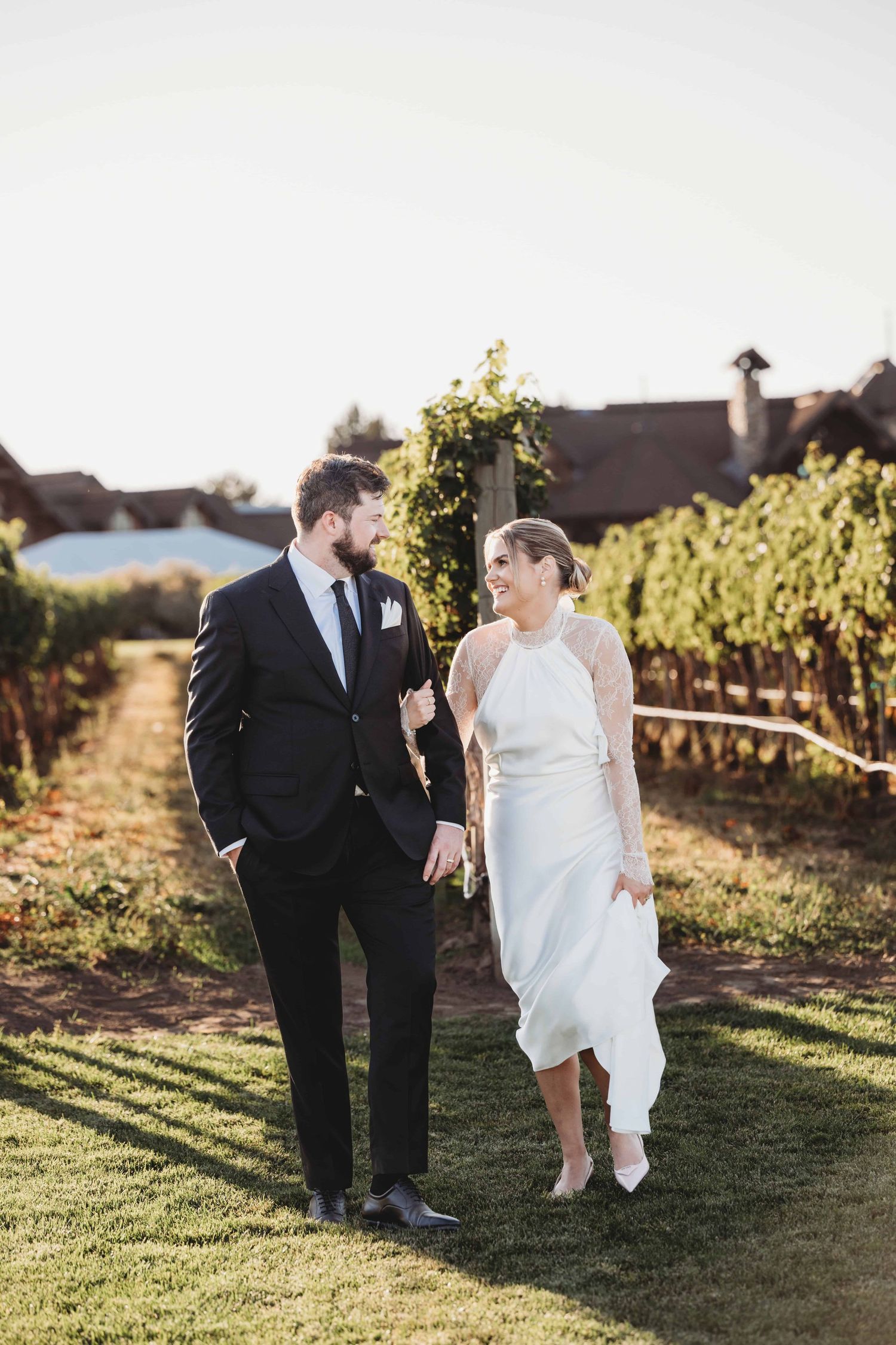A bride and groom walking through a vineyard and laughing after their wedding ceremony.