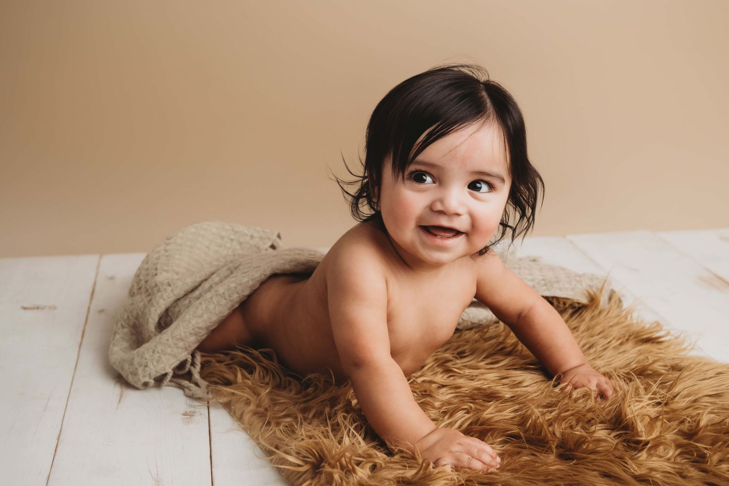 A baby laying on a white wood floor with a brown blanket.