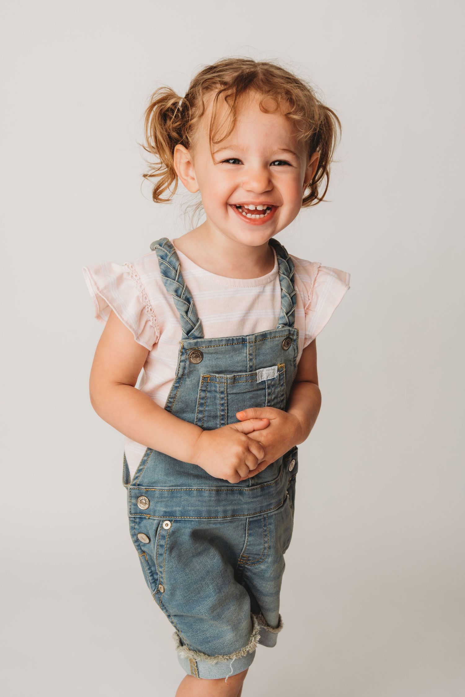A girl in jean overalls laughing on a white backdrop in Walla Walla.