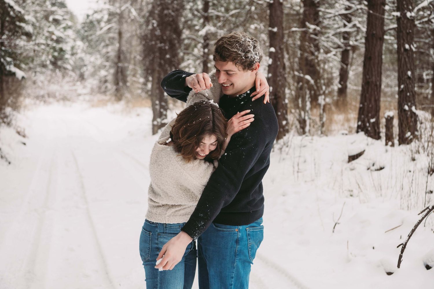 A man throwing snow on his fiance's head in a playful couples portrait.