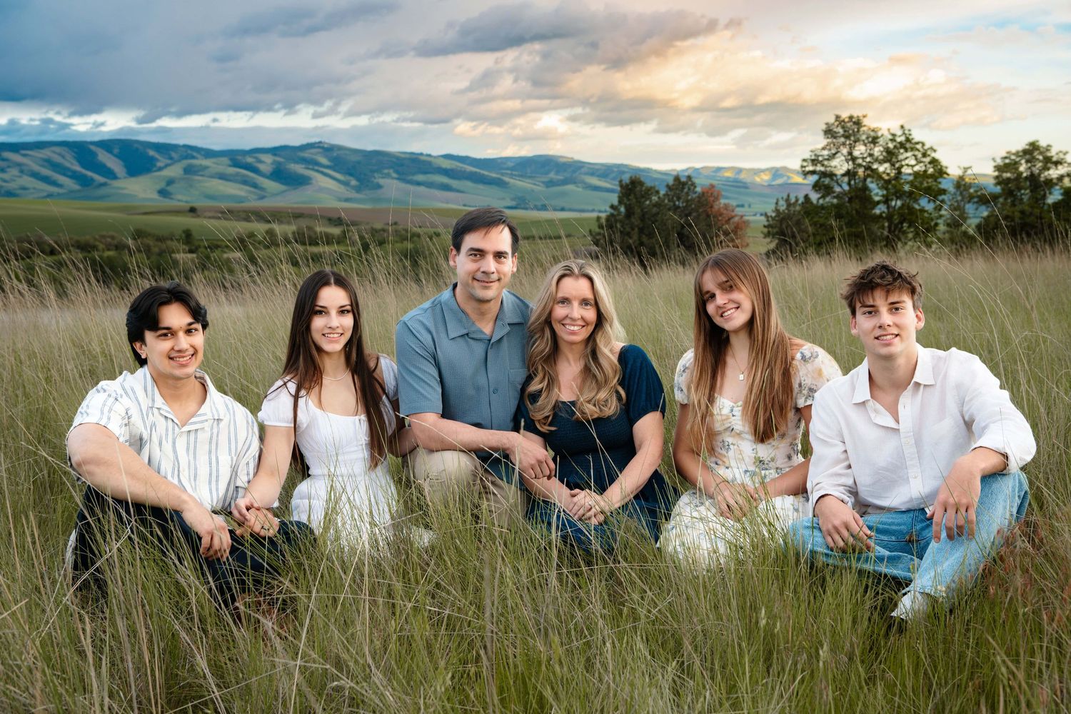 A family sitting surrounded by tall grasses and a dramatic colorful sunset.