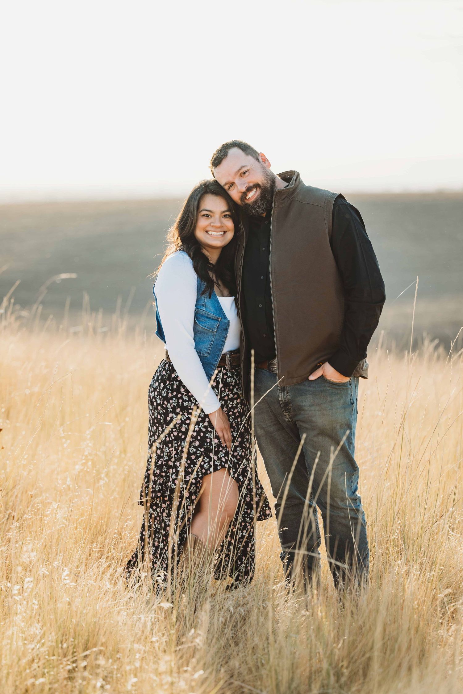 A couple standing in tall golden grasses looking at the camera.