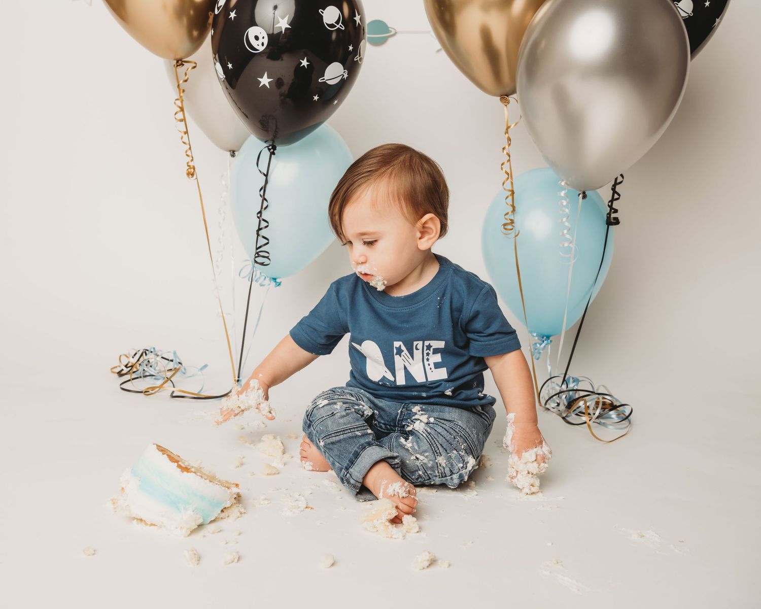 A one year old boy tips his cake off of the stand during his cake smash session at a Walla Walla studio.