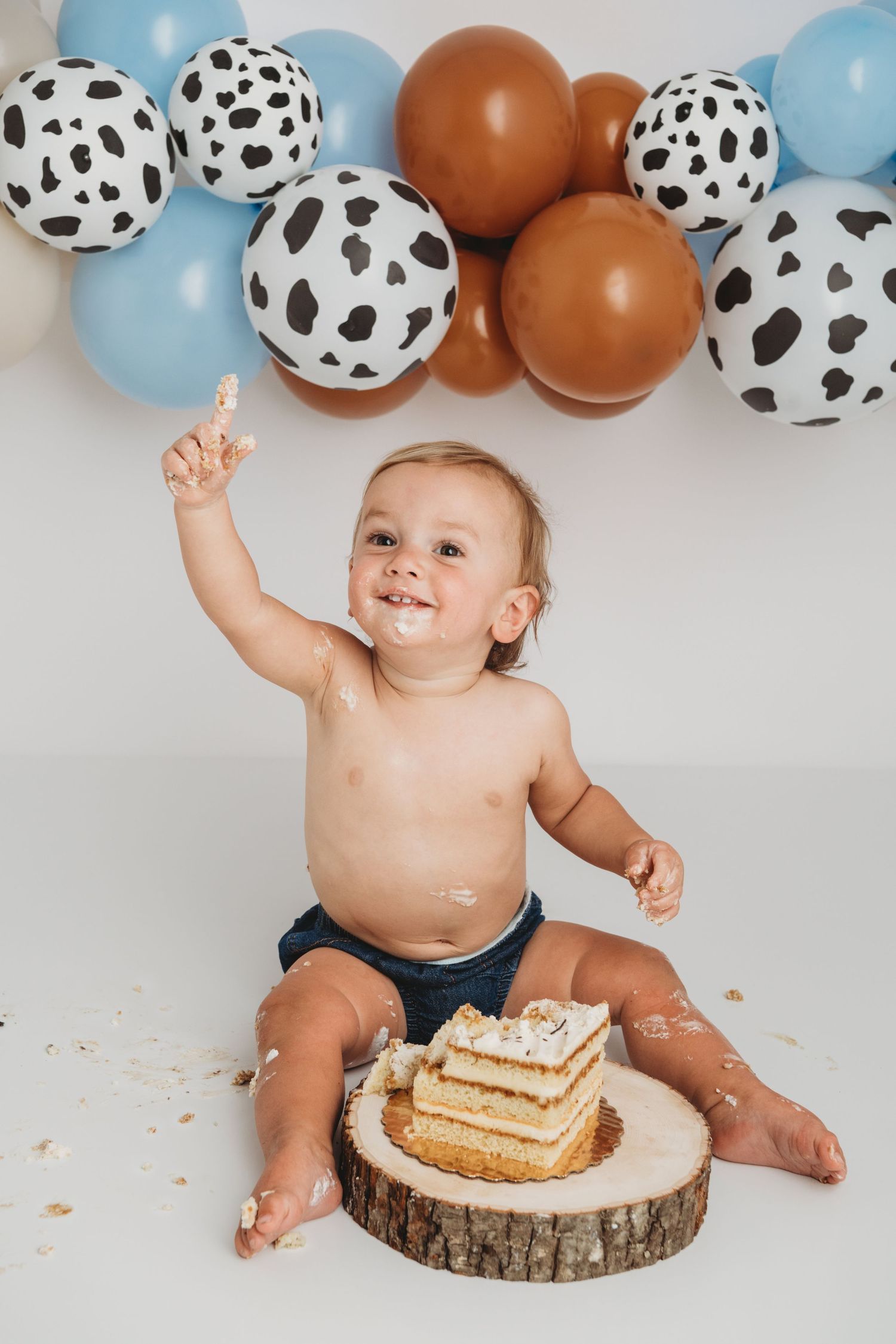 A portrait of a one year old boy with a cow print rodeo themed ballon garland.