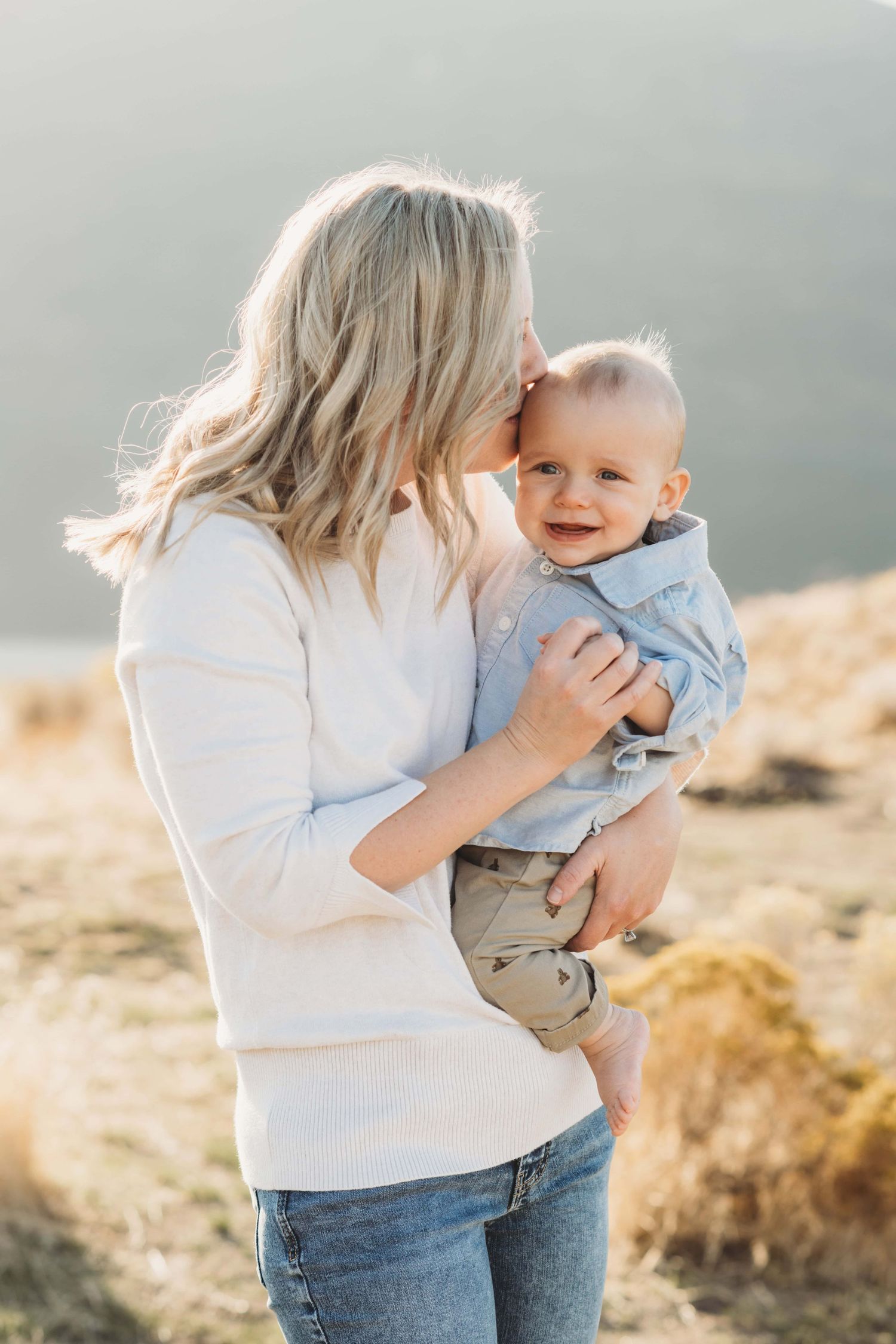 A mother holding her baby and kissing his head while he smiles.